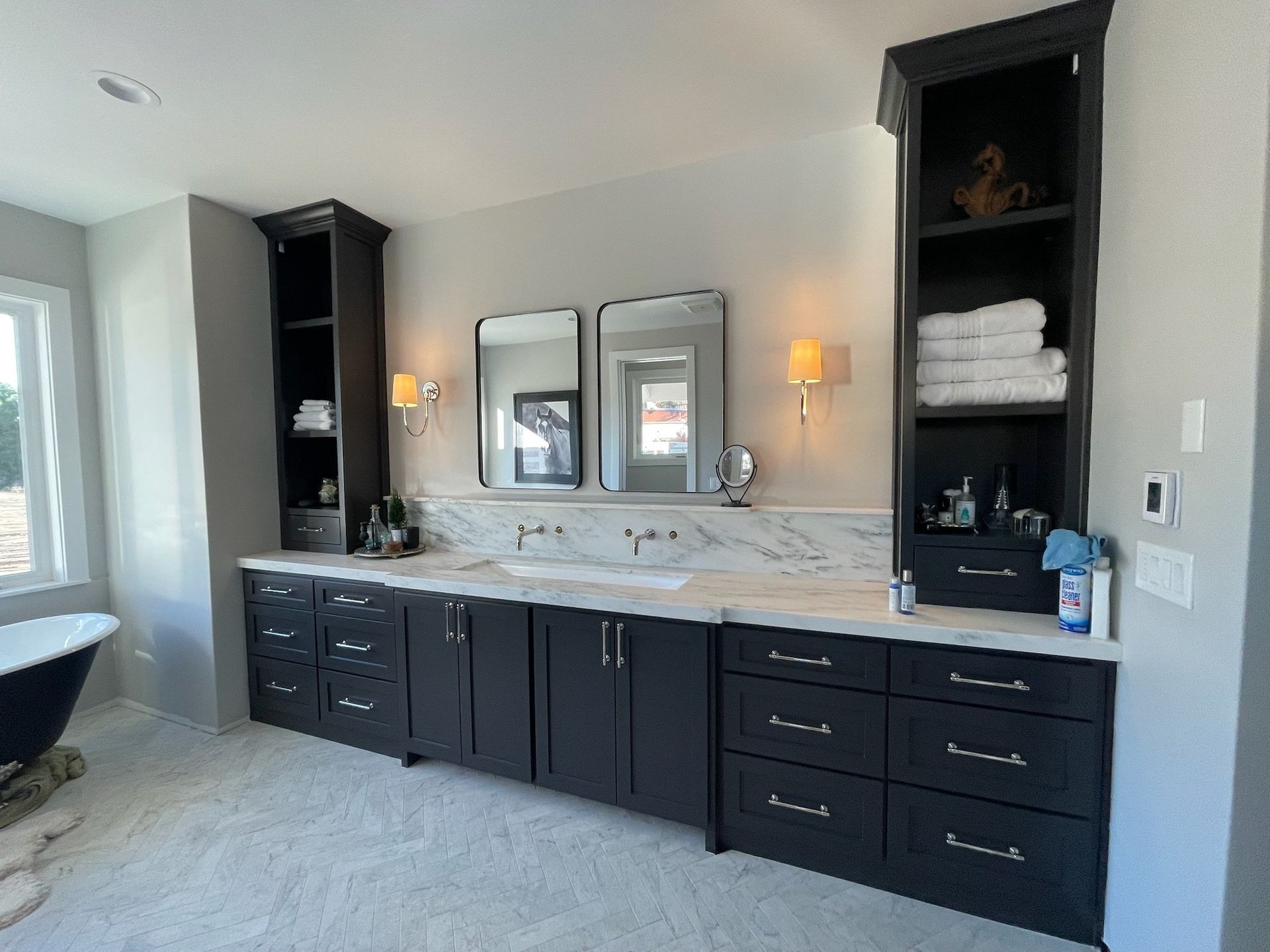 Modern bathroom vanity with black cabinets, marble countertop, mirrors, sconces, and shelving.
