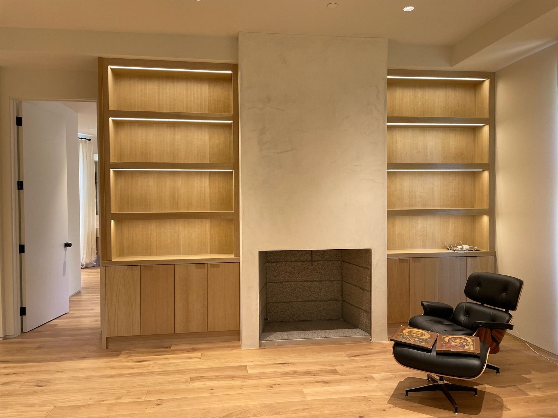Living room with built-in bookshelves, central fireplace, wood floors, and a black chair in front.