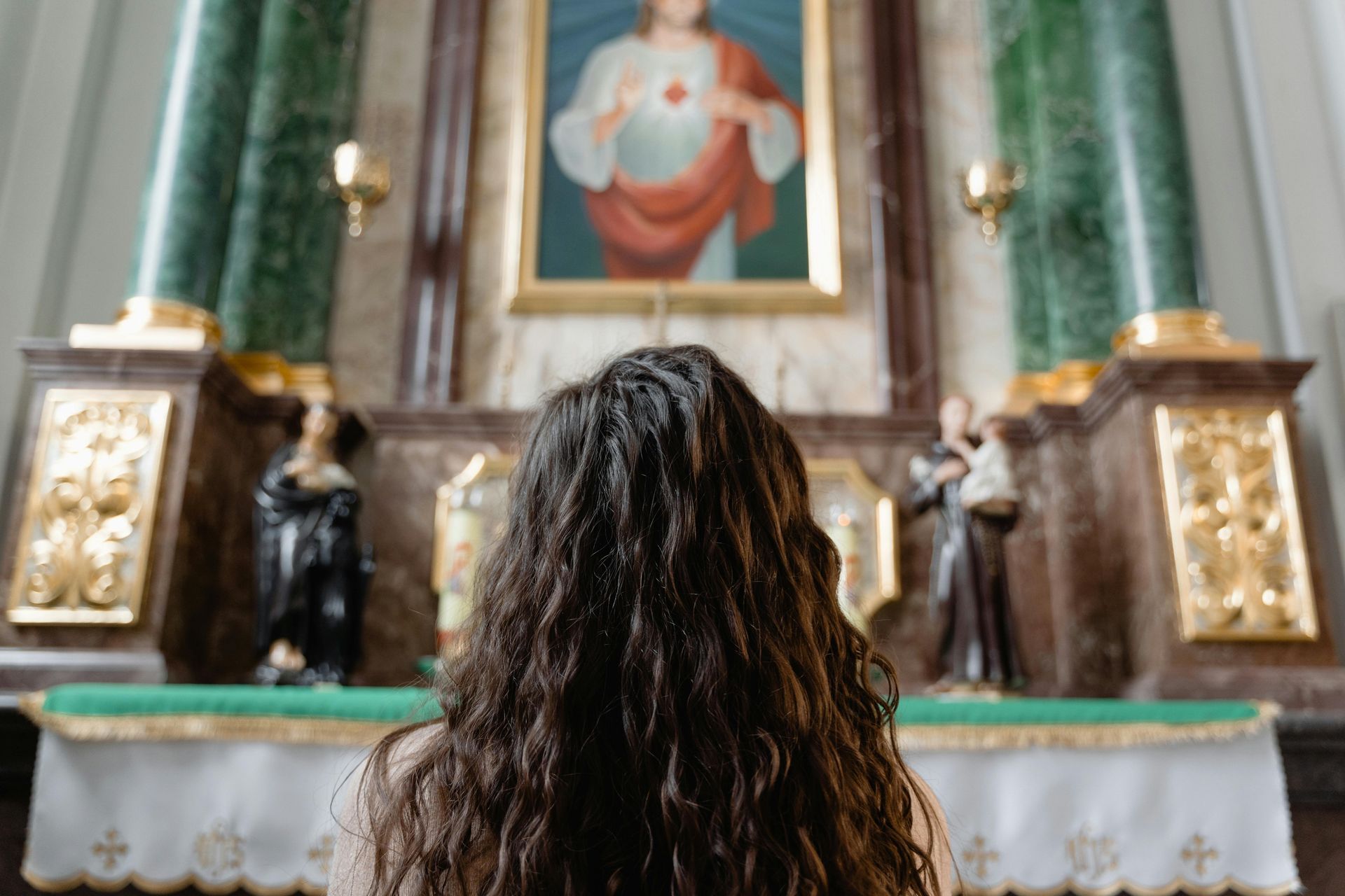 A woman is sitting in front of an altar in a church looking at a painting of jesus.