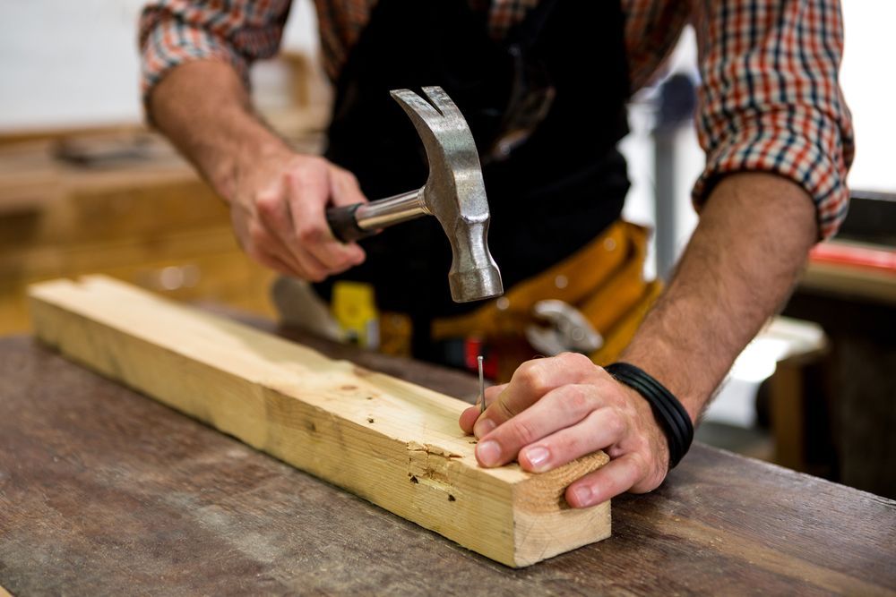 Person hammering a nail into a wooden plank on a workbench