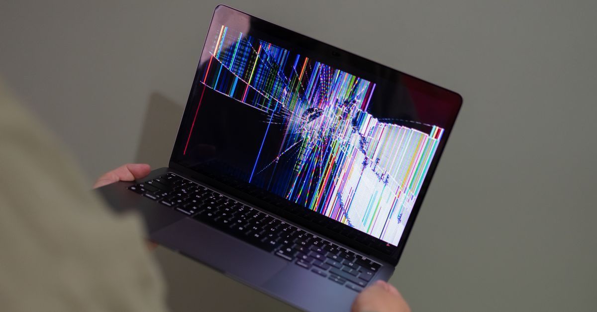 Pantalla de portátil con coloridas líneas verticales distorsionadas, sostenida en las manos de alguien sobre un escritorio.
