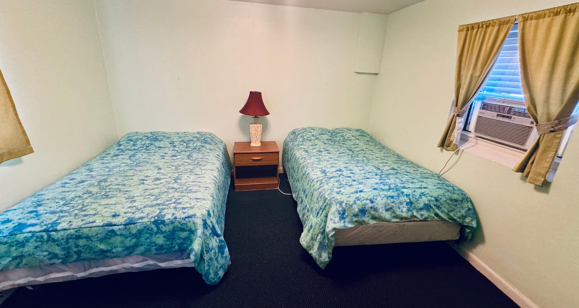 A bedroom with two beds , a nightstand , a lamp and a window.