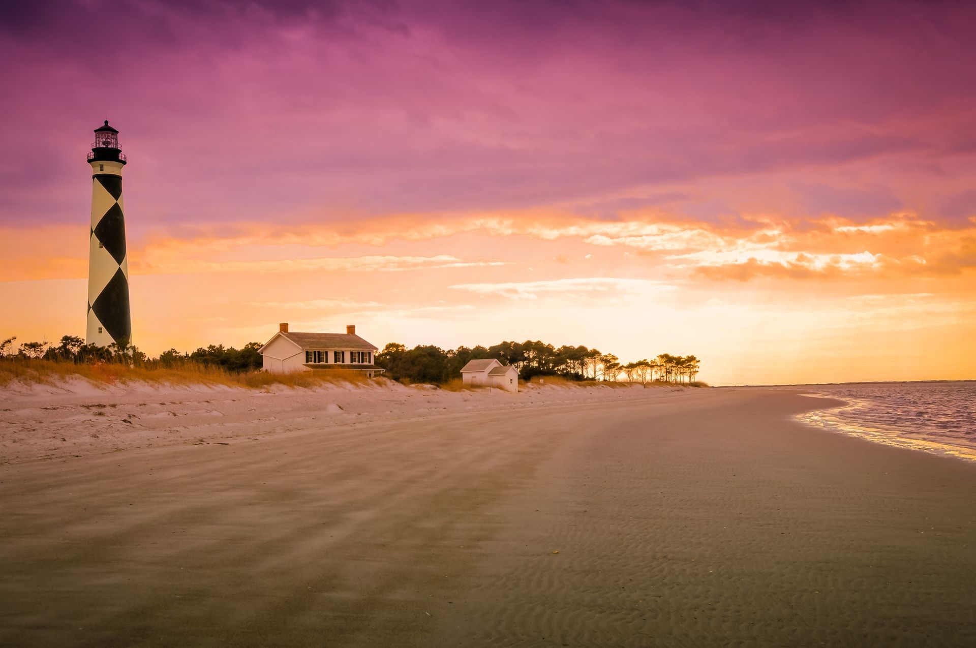There is a lighthouse on the beach at sunset.