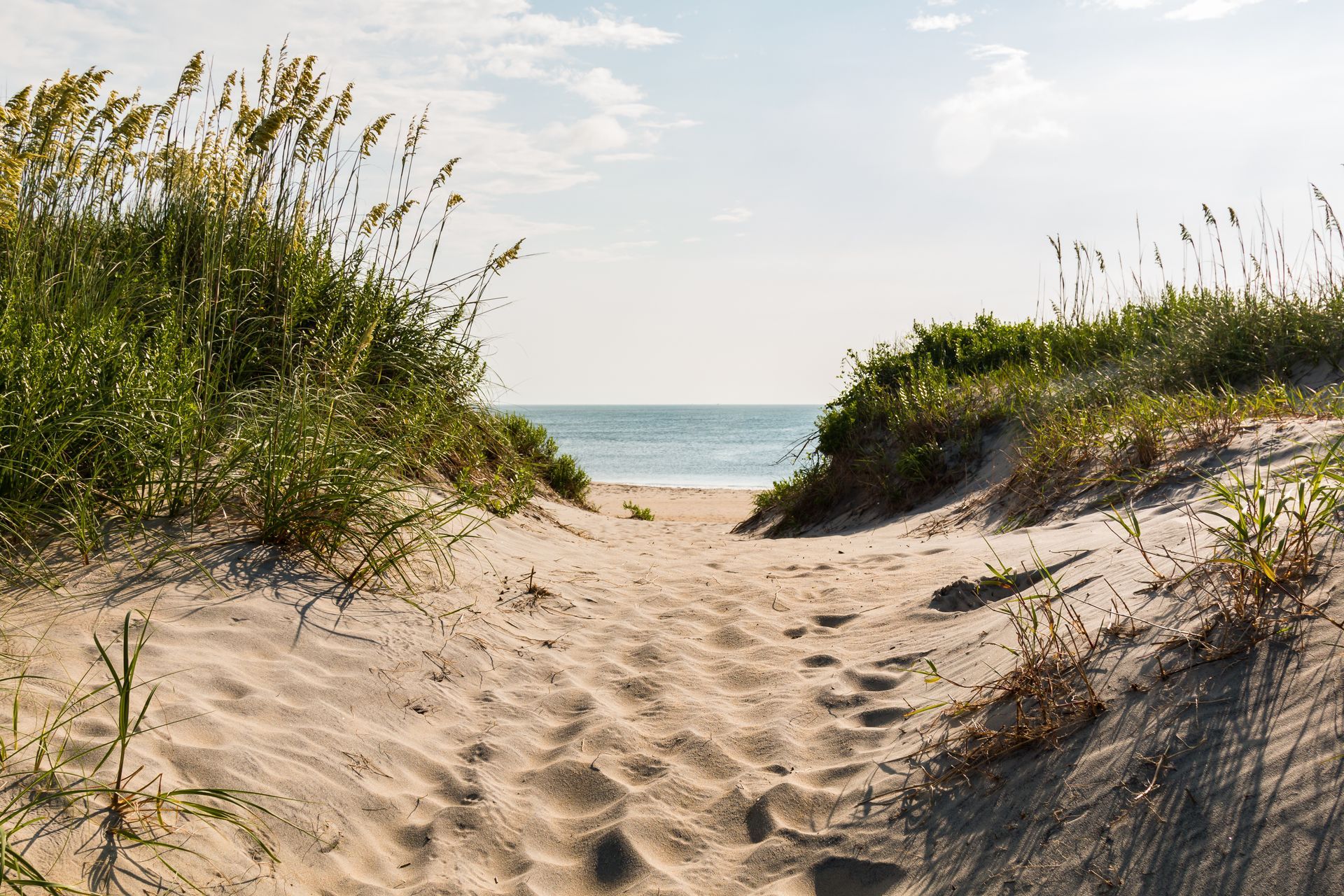 A sandy path leading to the beach with a view of the ocean.