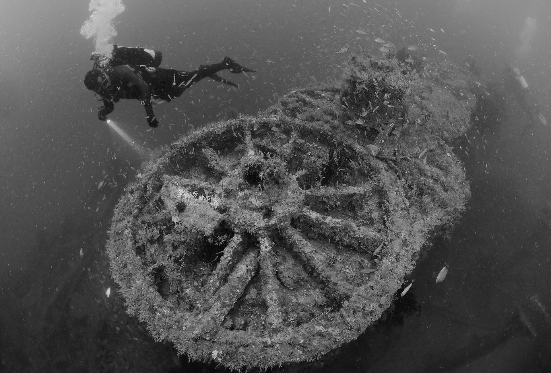 A black and white photo of two scuba divers near a large wheel in the water.