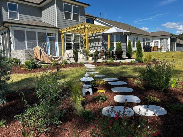 Backyard patio with yellow pergola, white stepping stones, and landscaped garden beside a suburban house