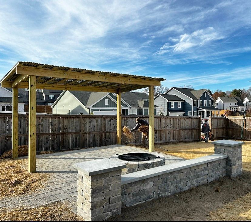 Backyard with a wooden pergola, stone fire pit, and fenced neighborhood houses under a blue sky