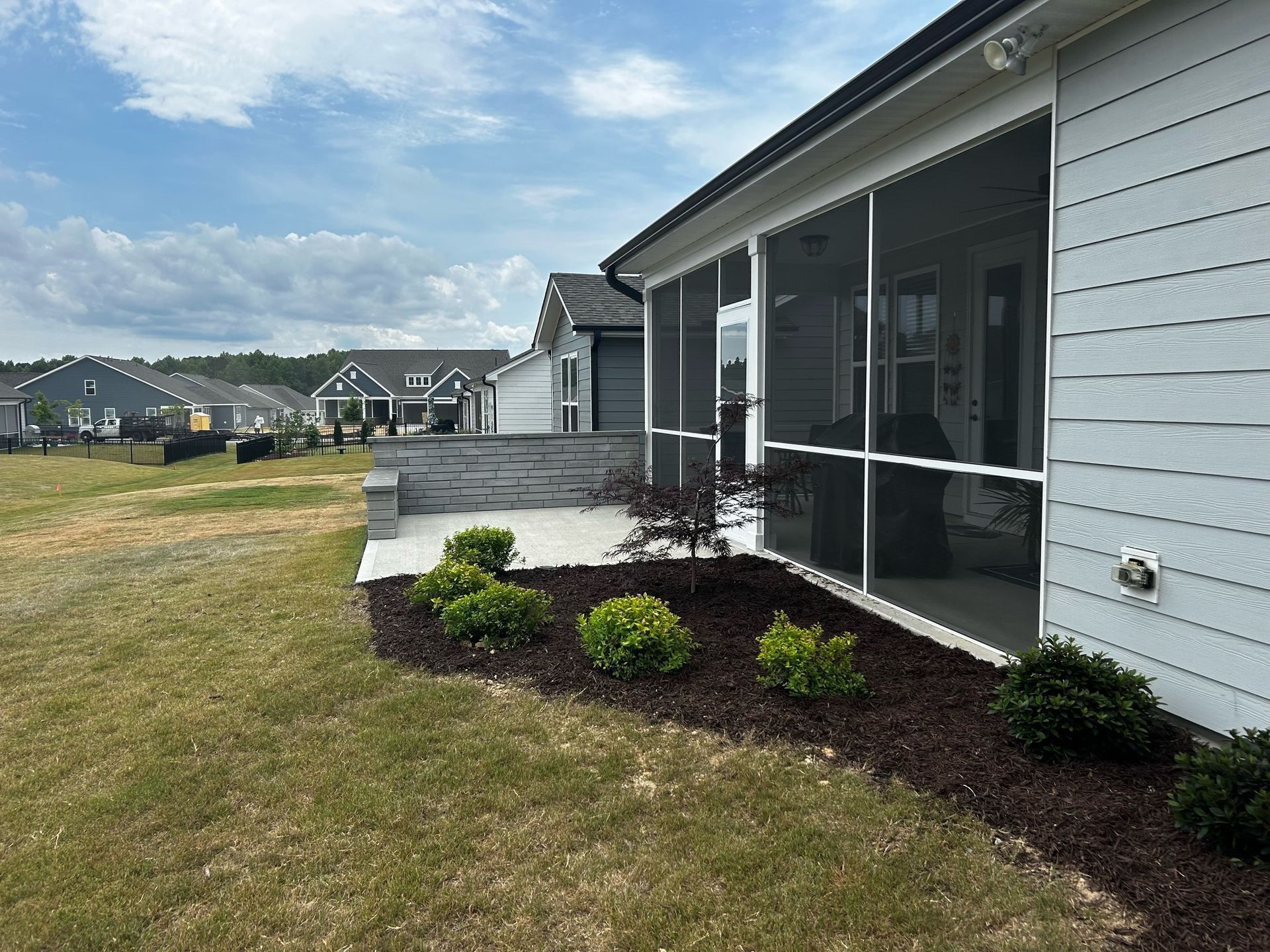 Single-story house exterior with screened porch, white siding, and a mulched flower bed along the lawn in Fuquay-Varina, NC