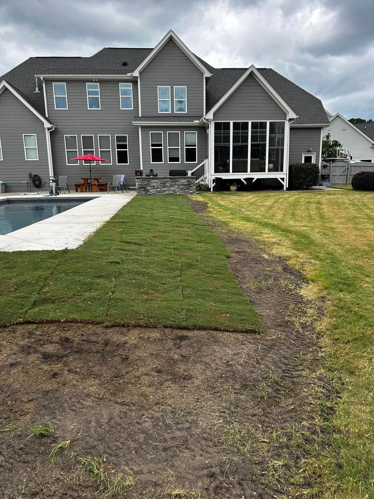 Suburban gray house with a wet lawn, gravel driveway, and patio after rain.