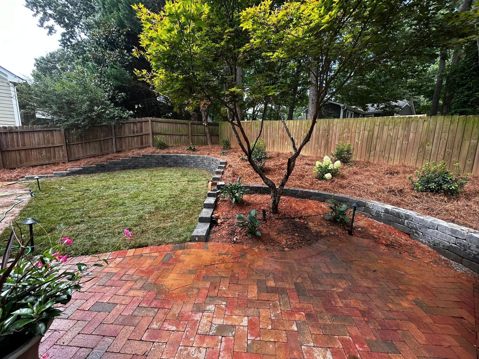 Brick patio with small tree, curved stone border, and fenced backyard garden in Cary, NC
