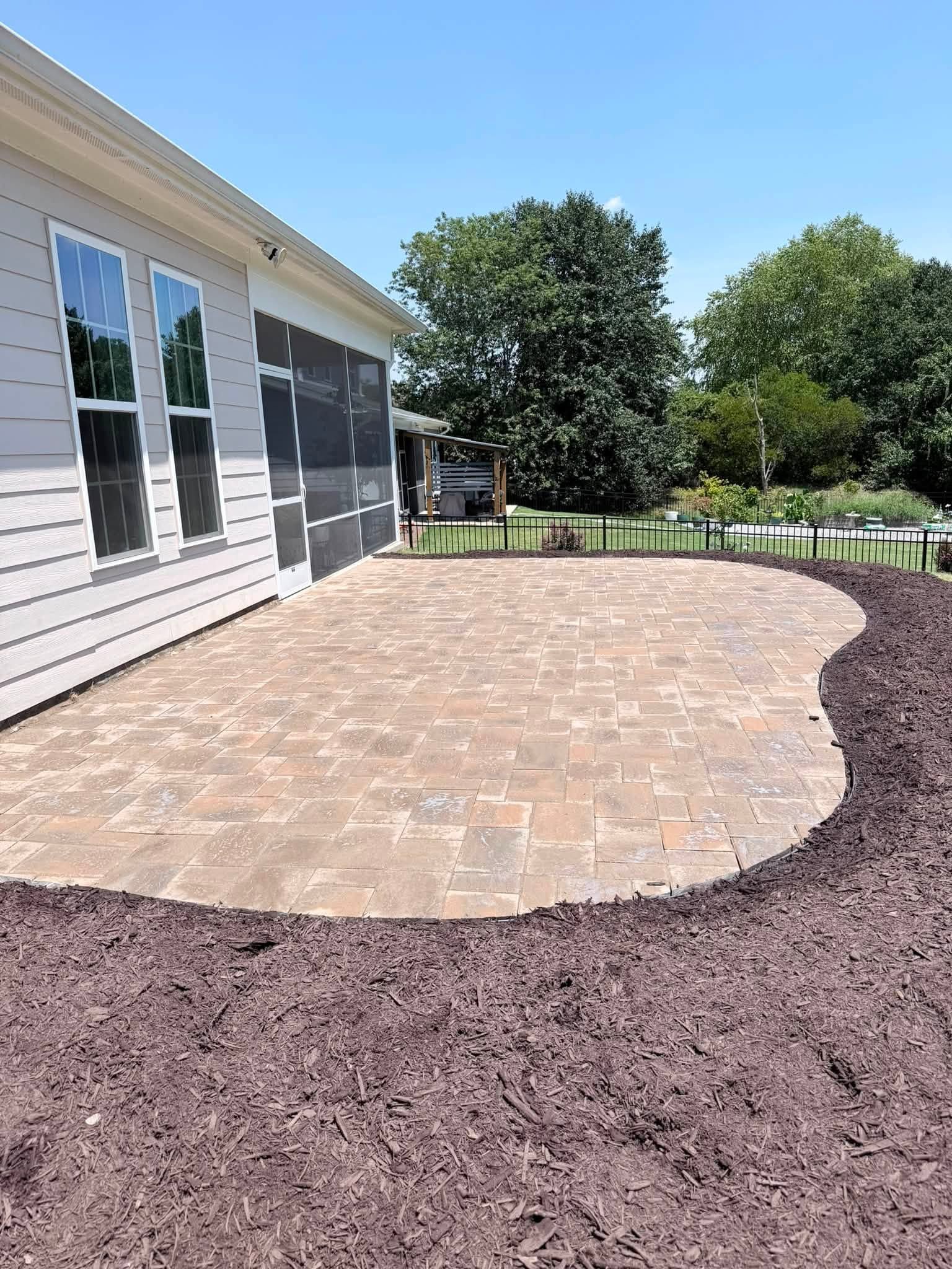 Back patio with brick pavers, gravel border, and a house exterior under a clear blue sky