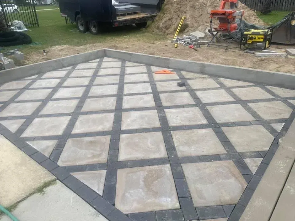 Backyard concrete patio with a gray grid pattern and large square pavers in the center
