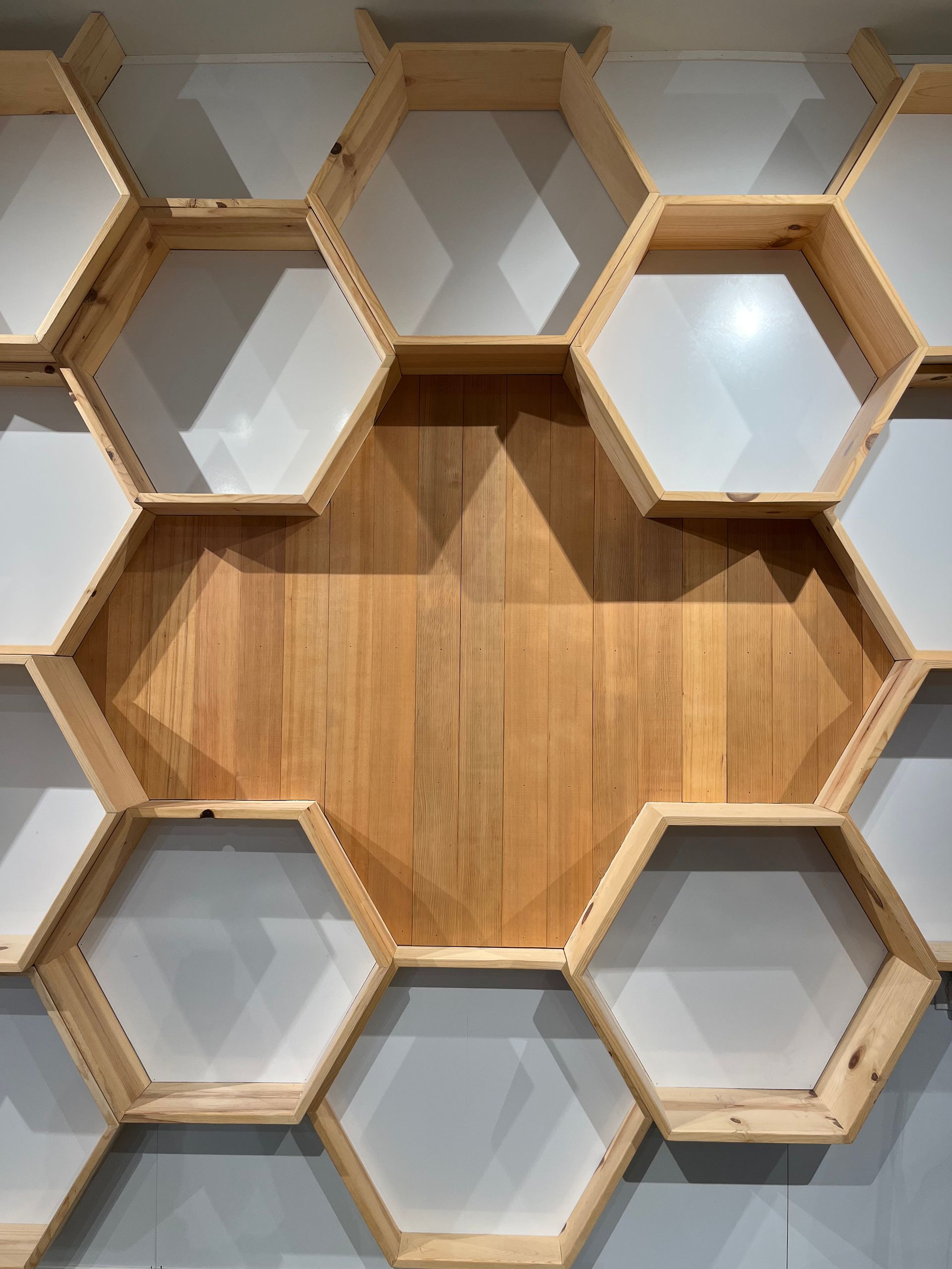 A wall-mounted display of connected wooden hexagonal shelves, featuring white backing and one large wooden-backed center.