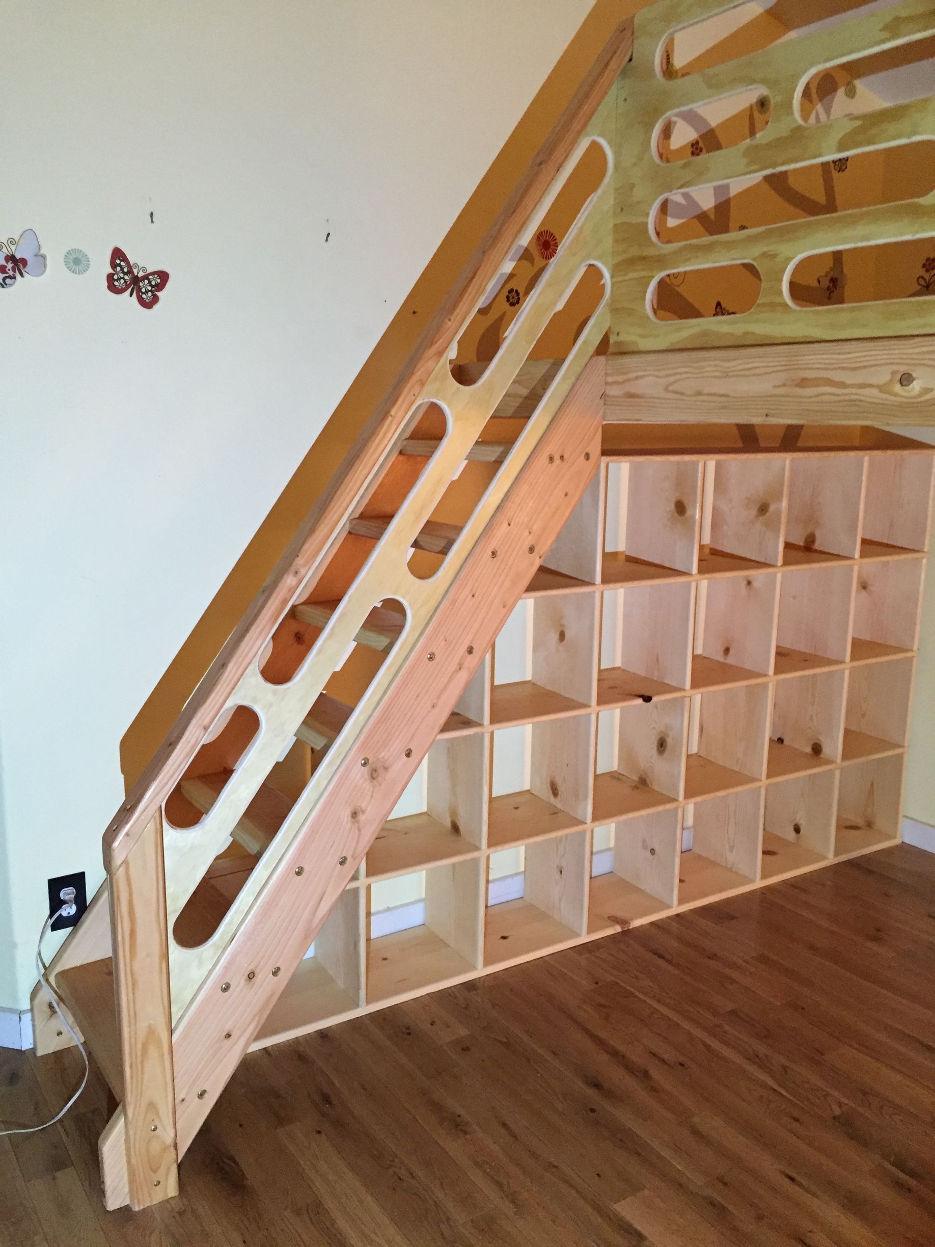 A wooden loft bed staircase with a built-in grid of storage cubbies underneath and decorative cutouts on the handrail.