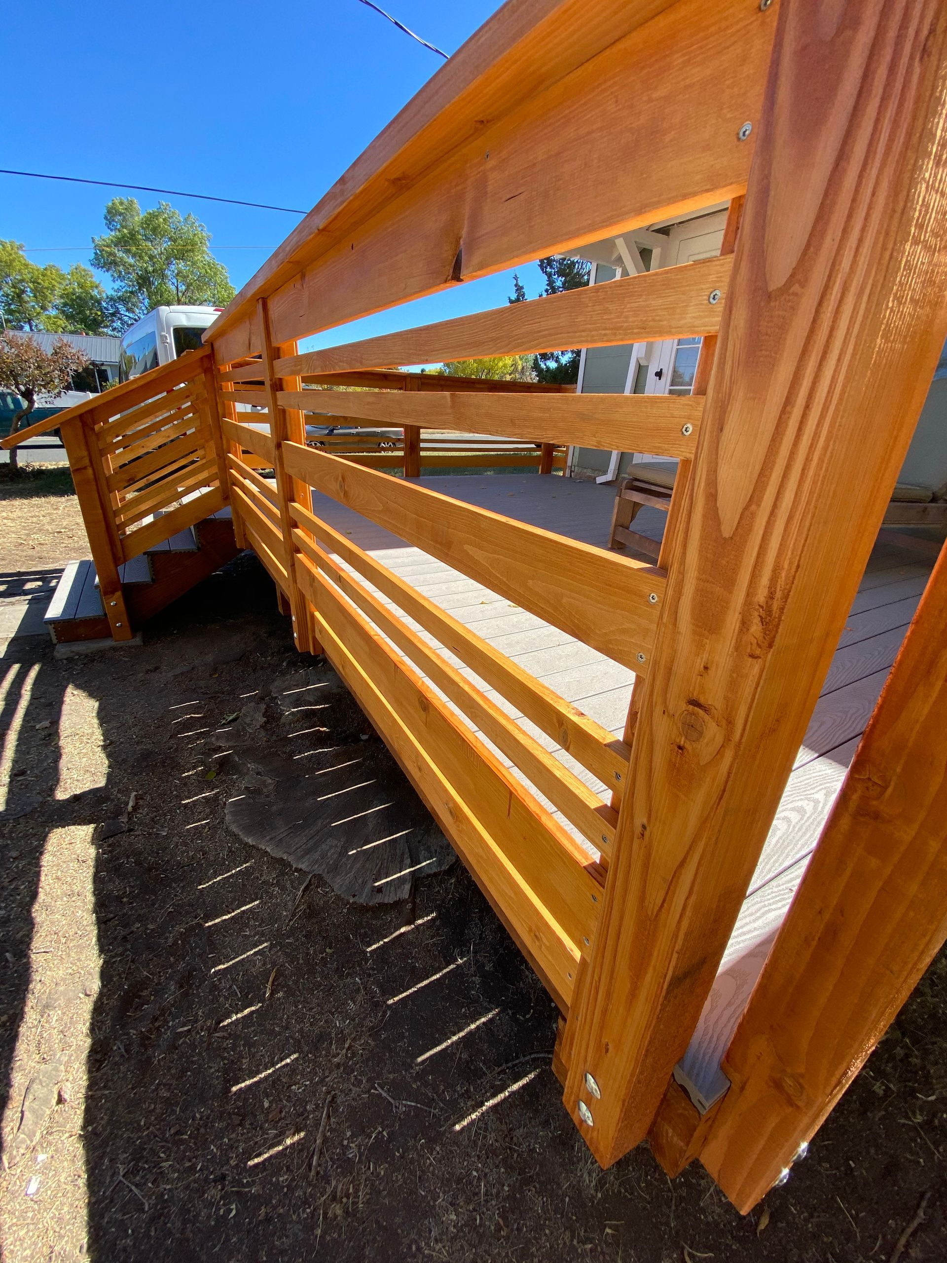 A wooden deck ramp with horizontal railings, viewed from the side on a sunny day.