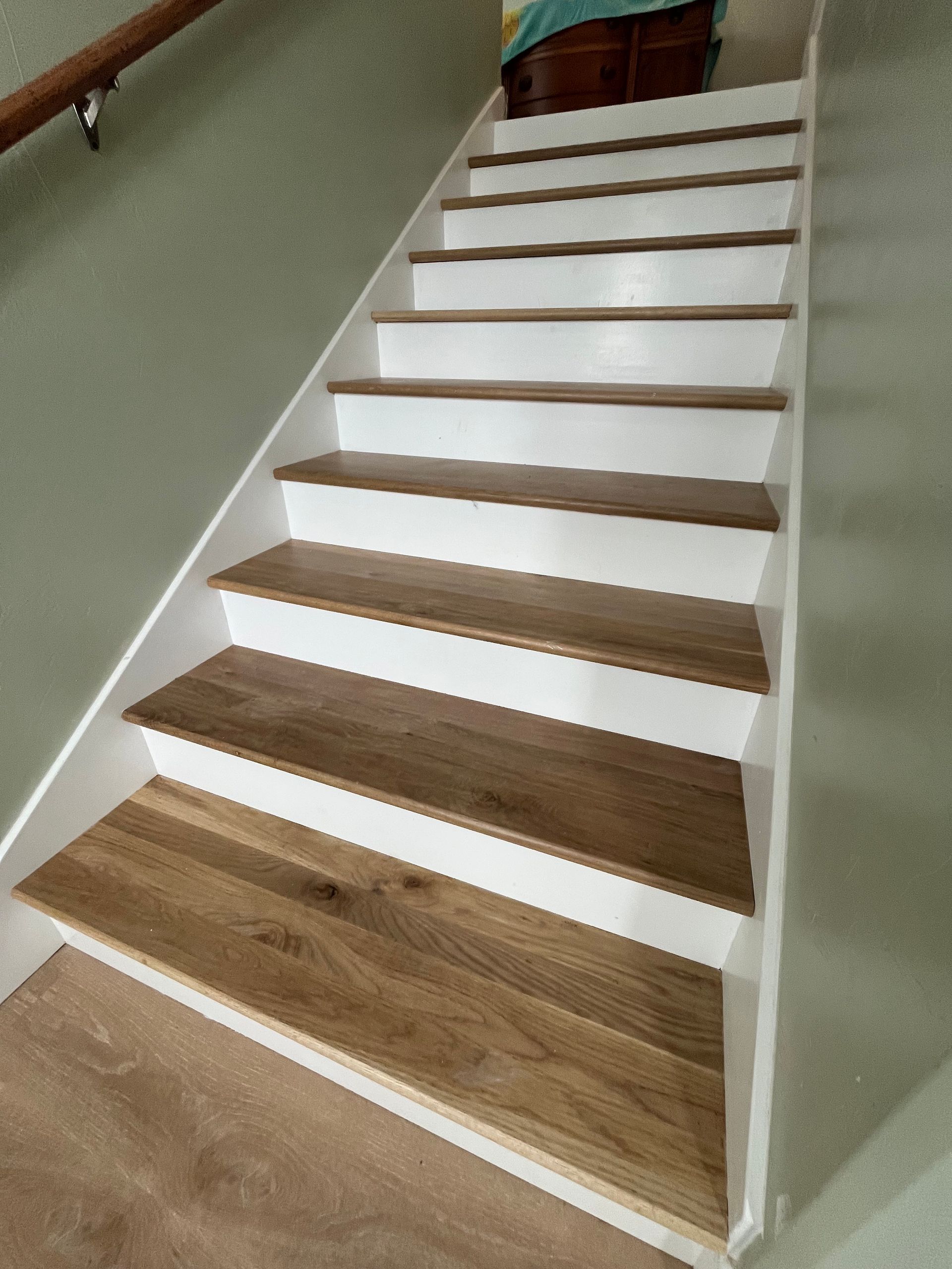 A staircase with wooden treads and white risers, viewed from the bottom looking up towards a landing.