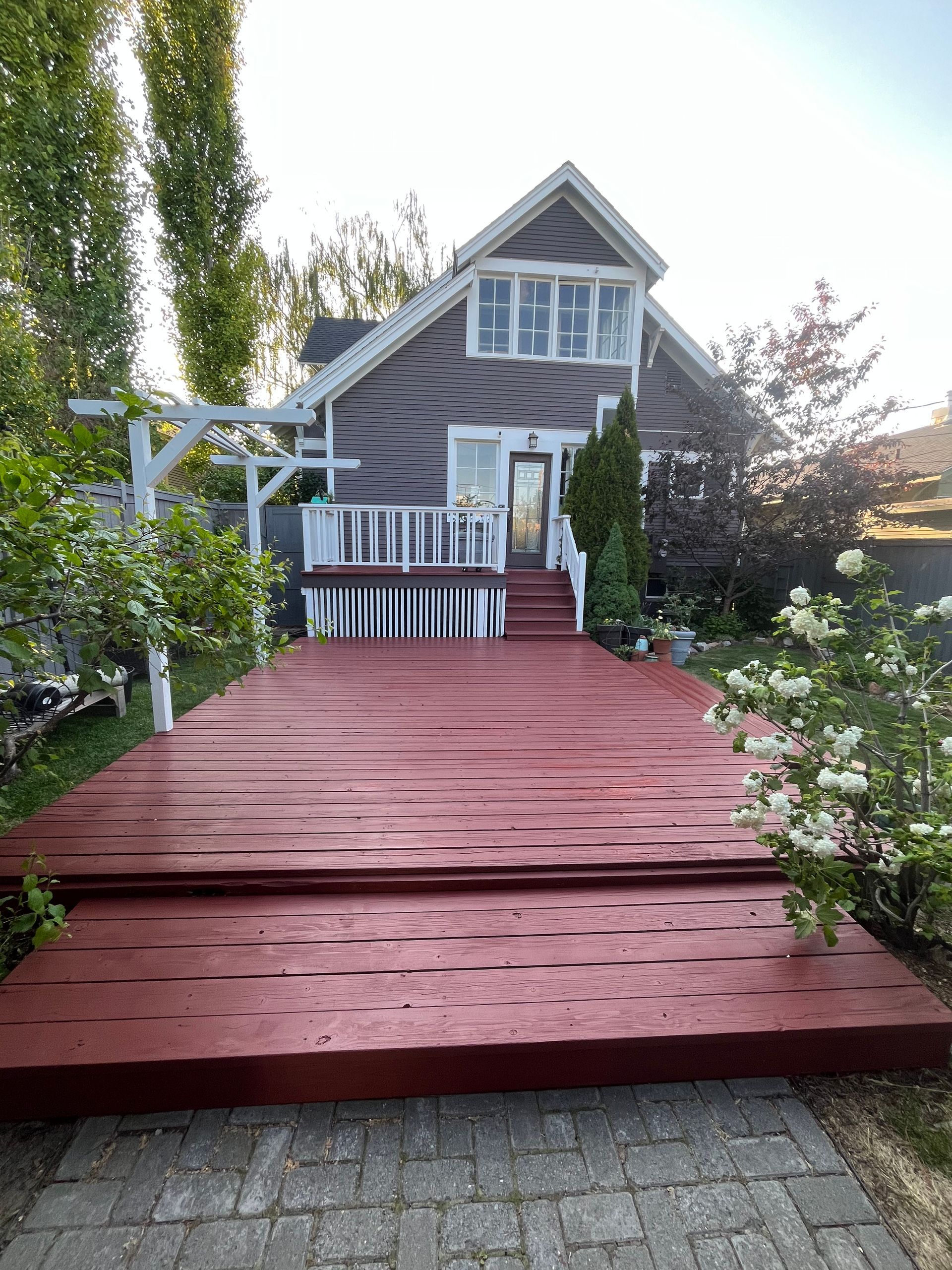 A large, freshly painted red wooden deck leads to the steps of a two-story gray house with white trim.