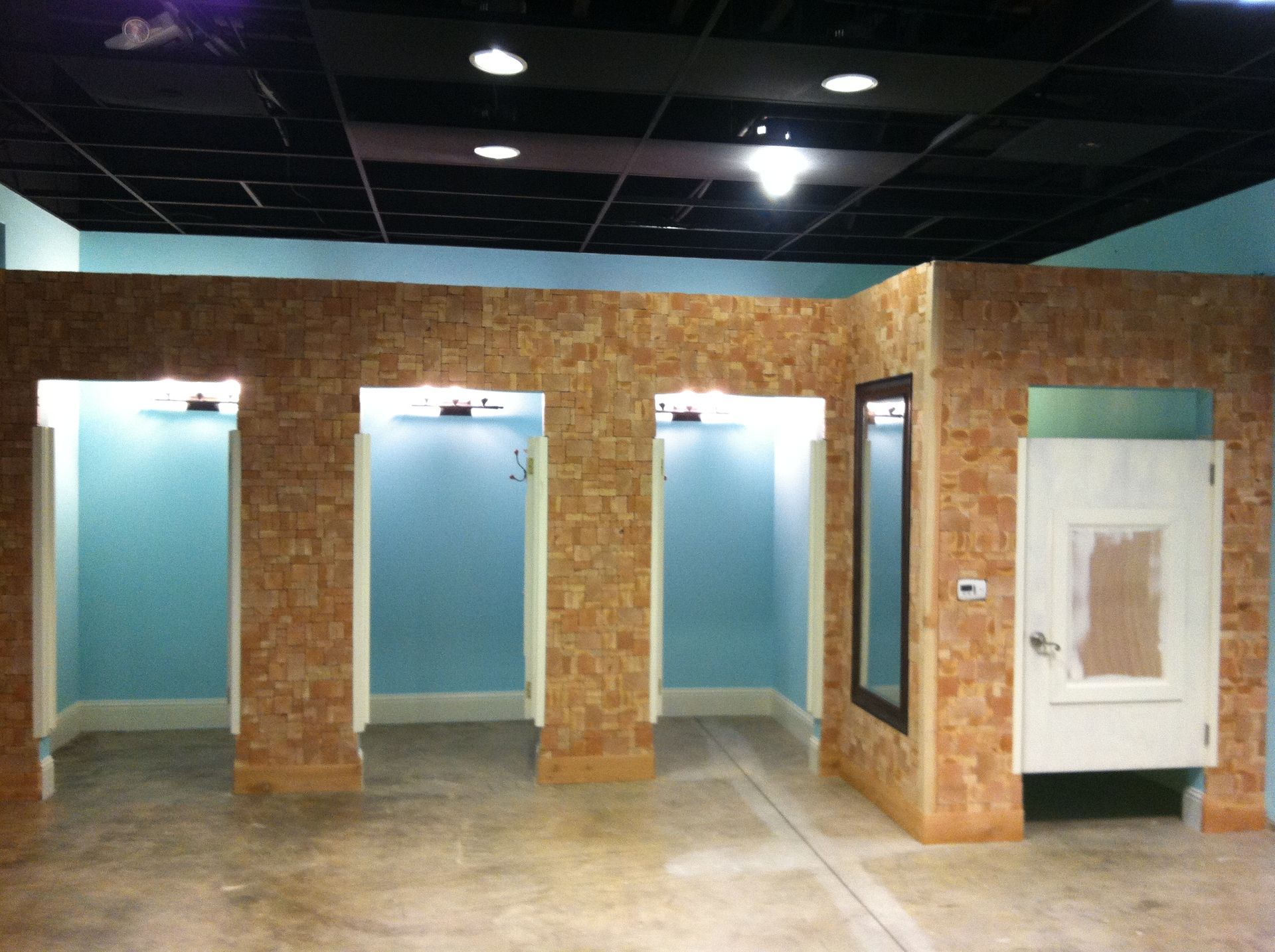 A row of dressing rooms with light blue walls and wood-textured partitions under a black drop ceiling.