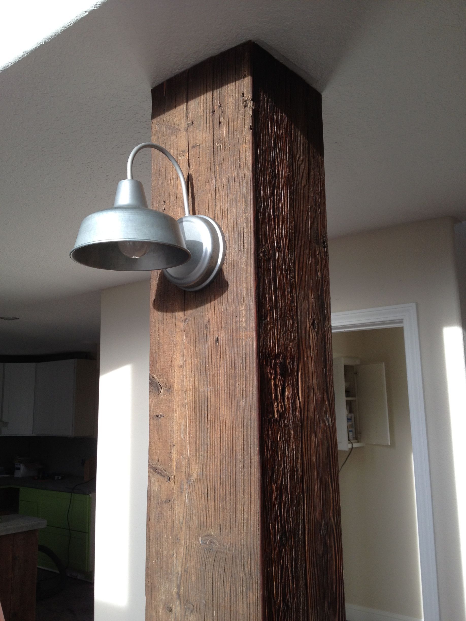 A metal industrial-style wall light fixture mounted on a rustic, weathered dark brown wooden support post.