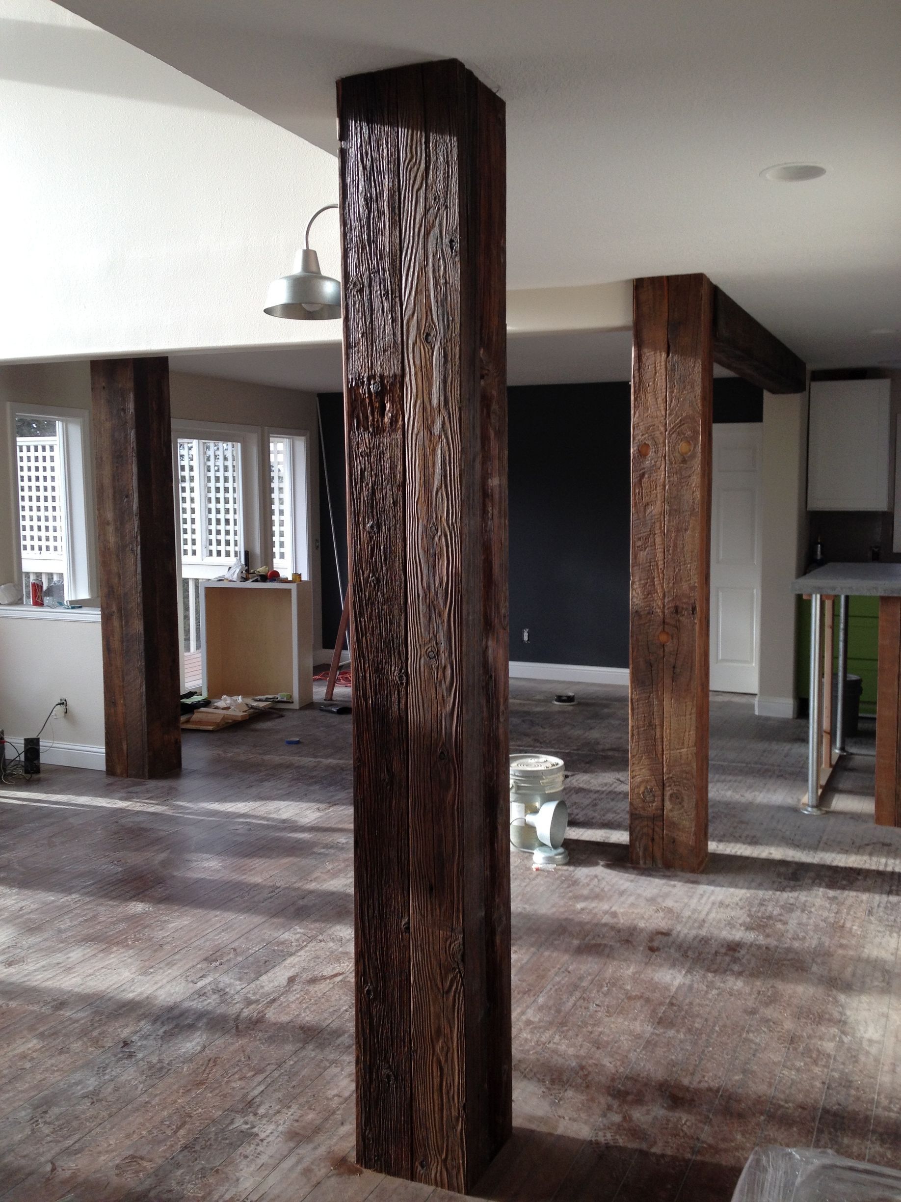 Three tall, dark, textured wooden posts stand in a bright, open-plan room undergoing renovation with exposed subflooring.
