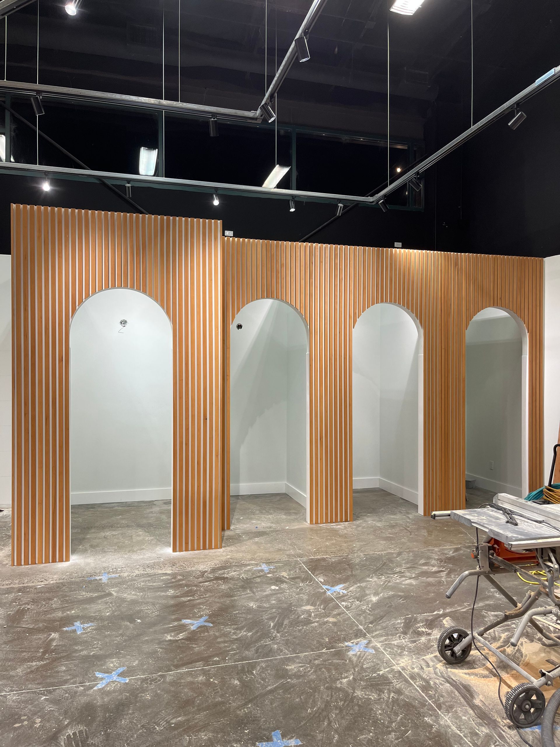 Four arched, wood-slatted room dividers stand in a construction area with a dusty floor and black ceiling.