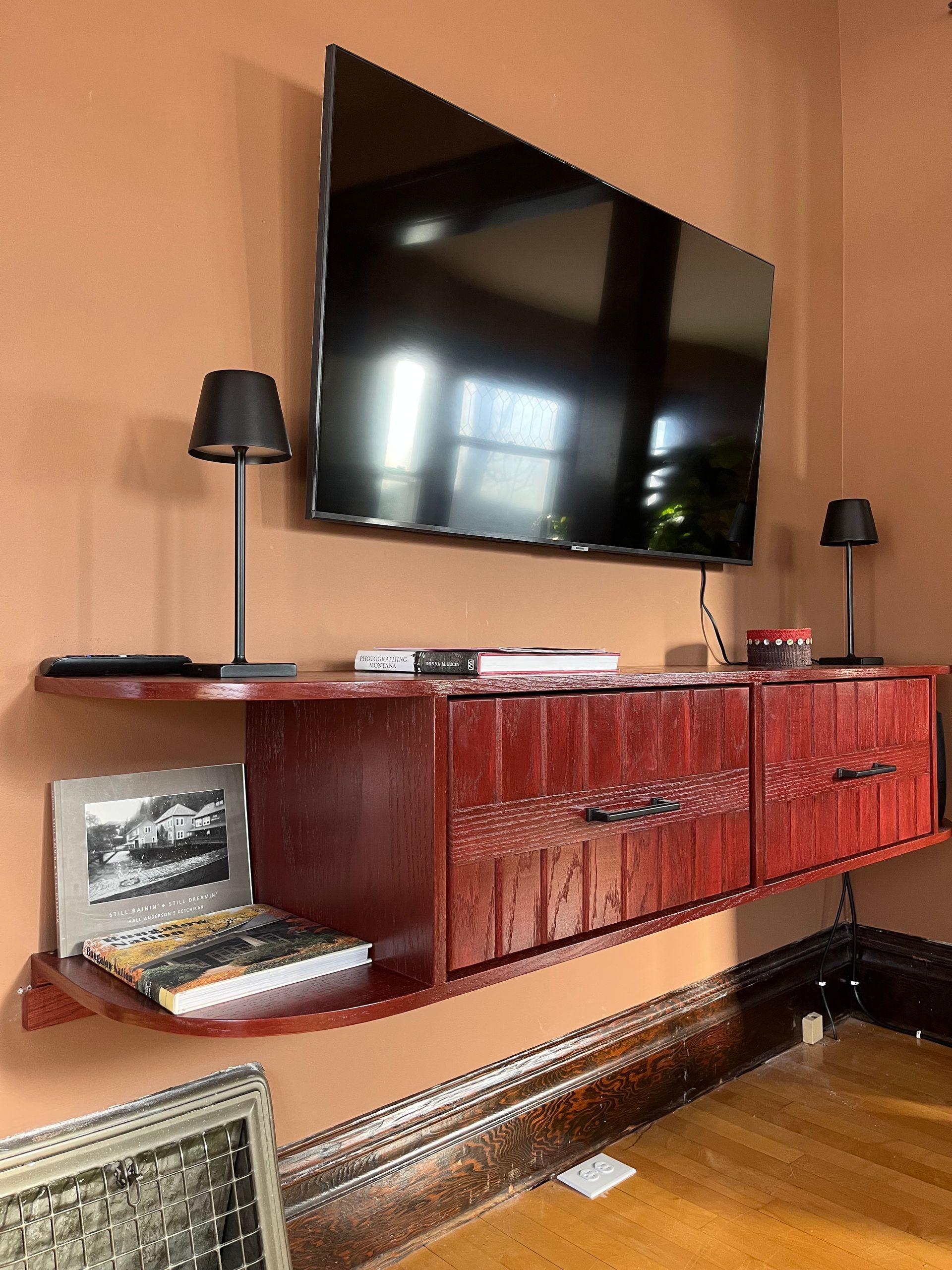 A dark wood floating console table with drawers and open shelving sits under a wall-mounted TV on a terracotta wall.