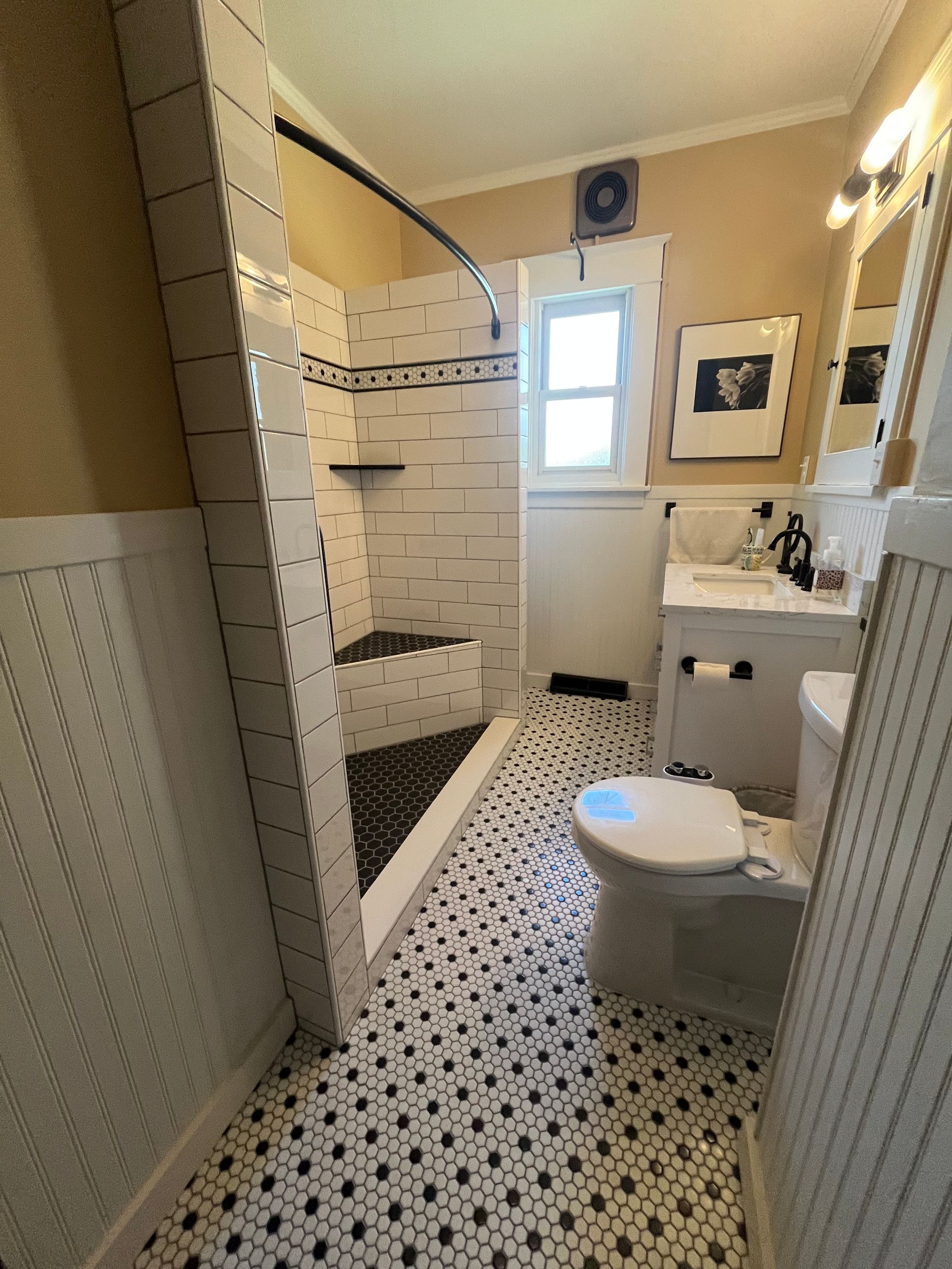 A small bathroom with a walk-in shower, black-and-white patterned tile flooring, a white toilet, and a vanity sink.