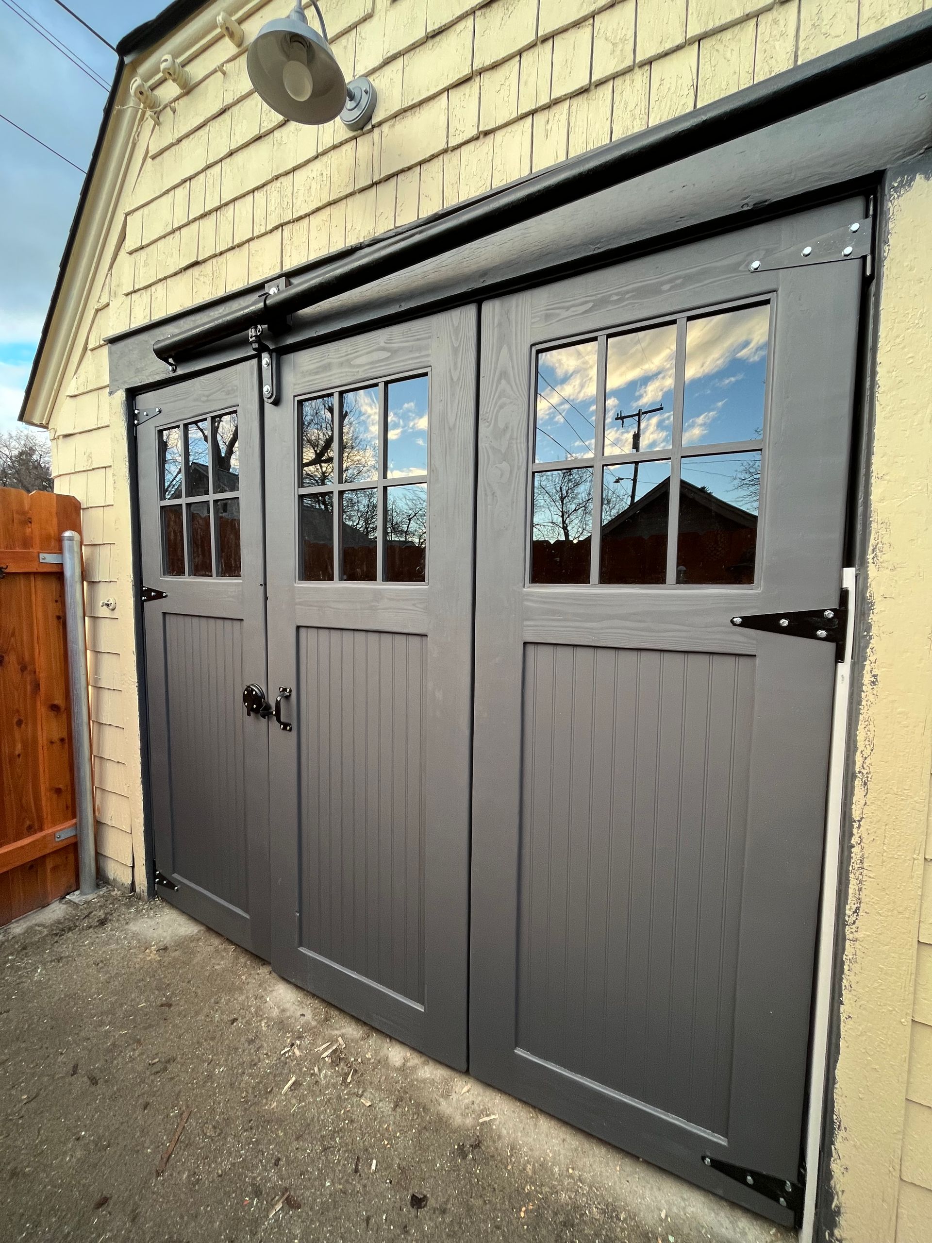 Dark grey double doors with square window panes and black hardware on a light-colored shed with exterior lighting.