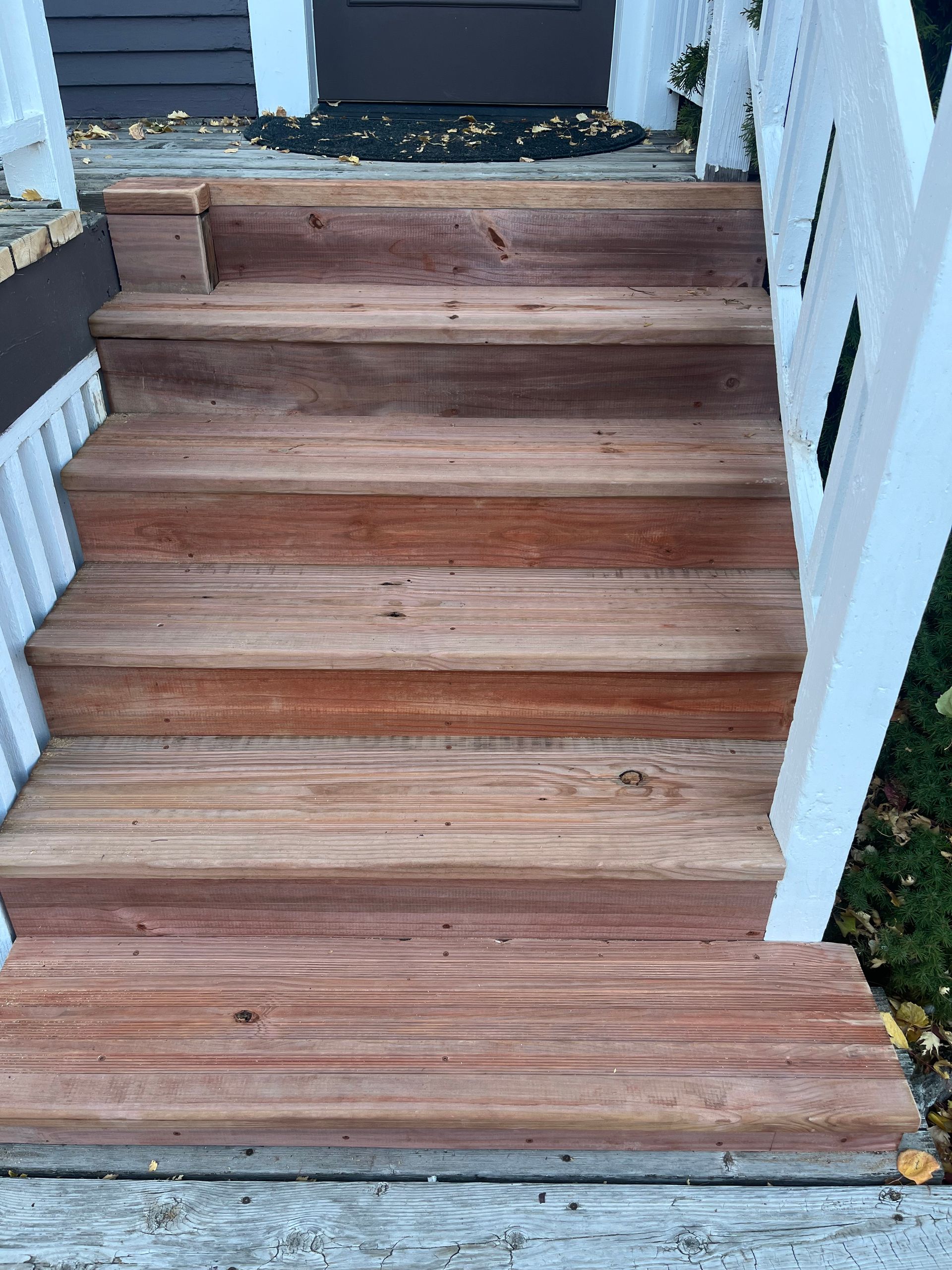 A set of five wooden outdoor steps leading up to a house entrance with white railings on either side.