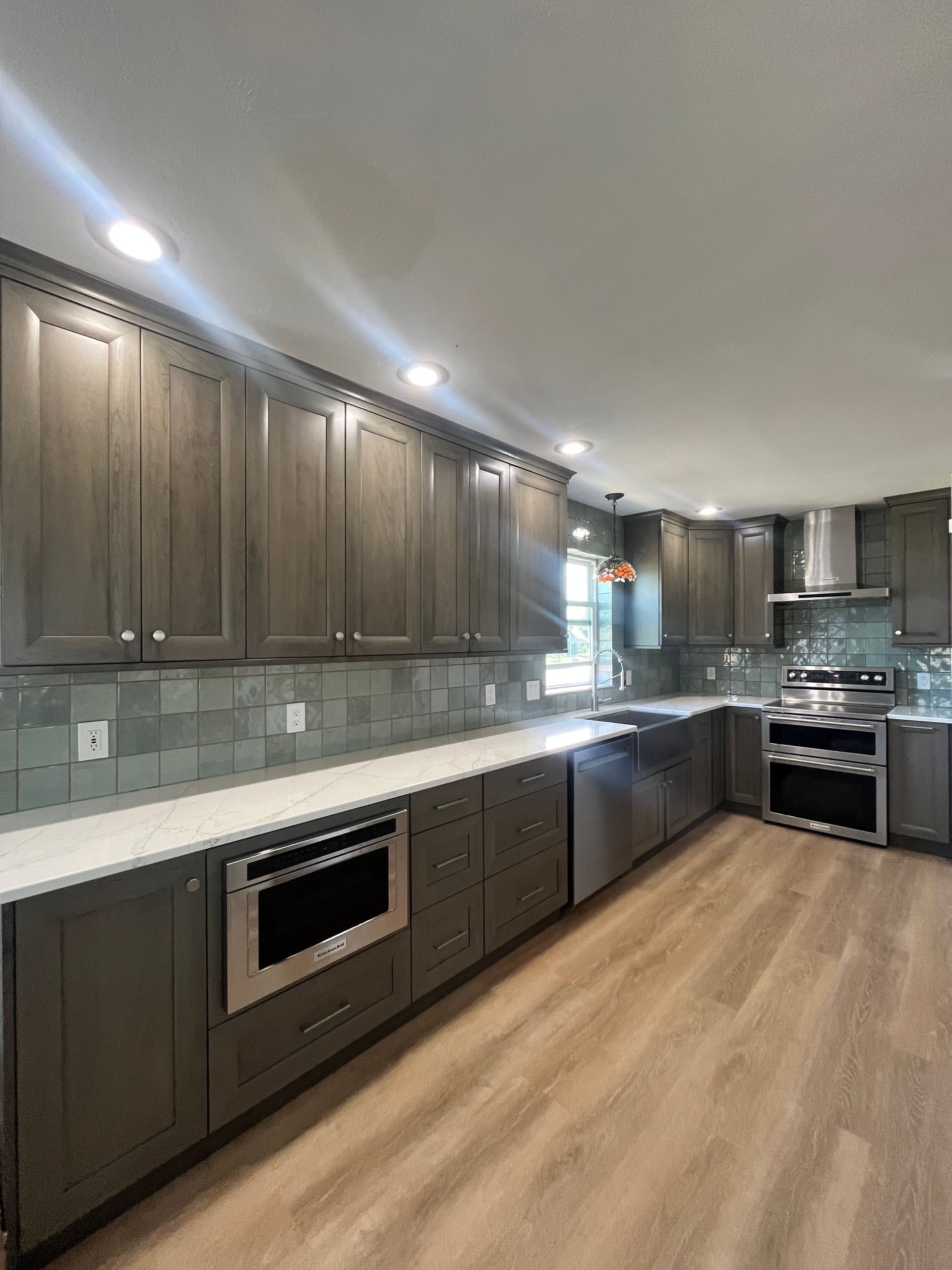 Modern kitchen with dark wood cabinets, white countertops, stainless steel appliances, and wood-look flooring.