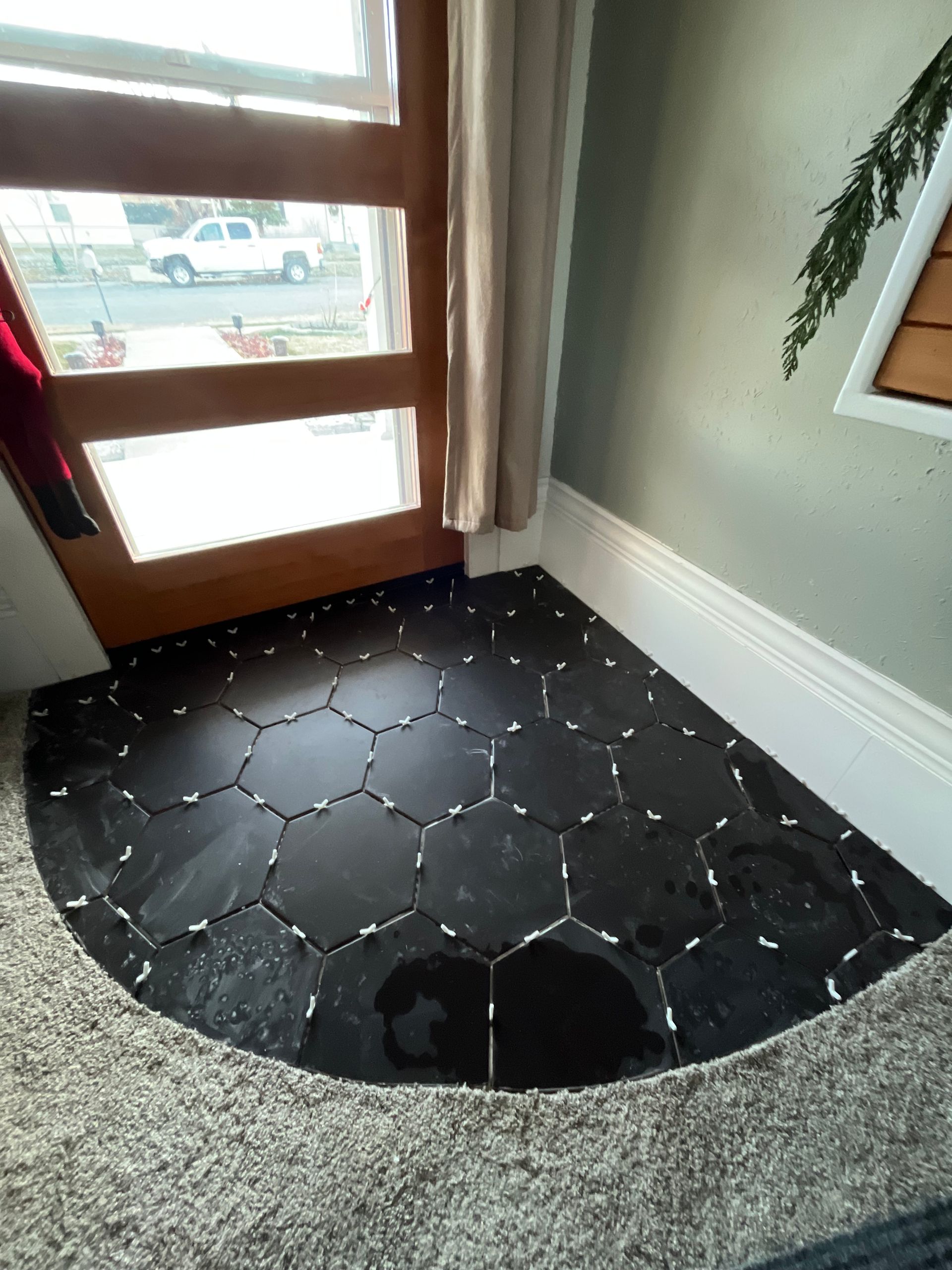 Black hexagon floor tiles partially installed in a foyer, featuring white plastic spacers between them.