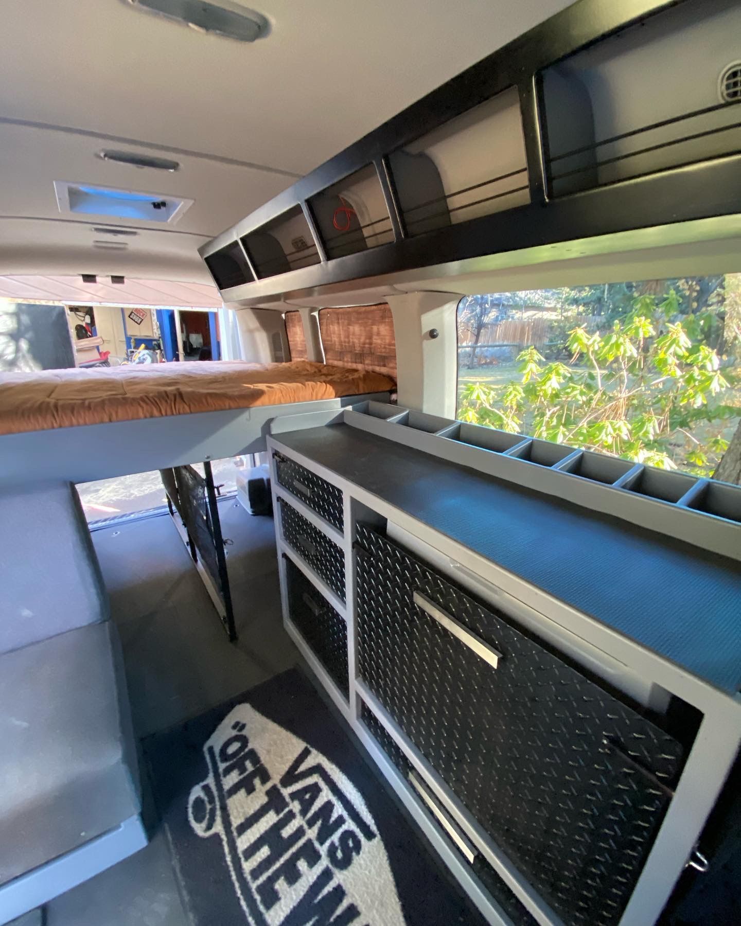 Interior of a converted van featuring a bed, storage cabinets, a dark countertop, and a 