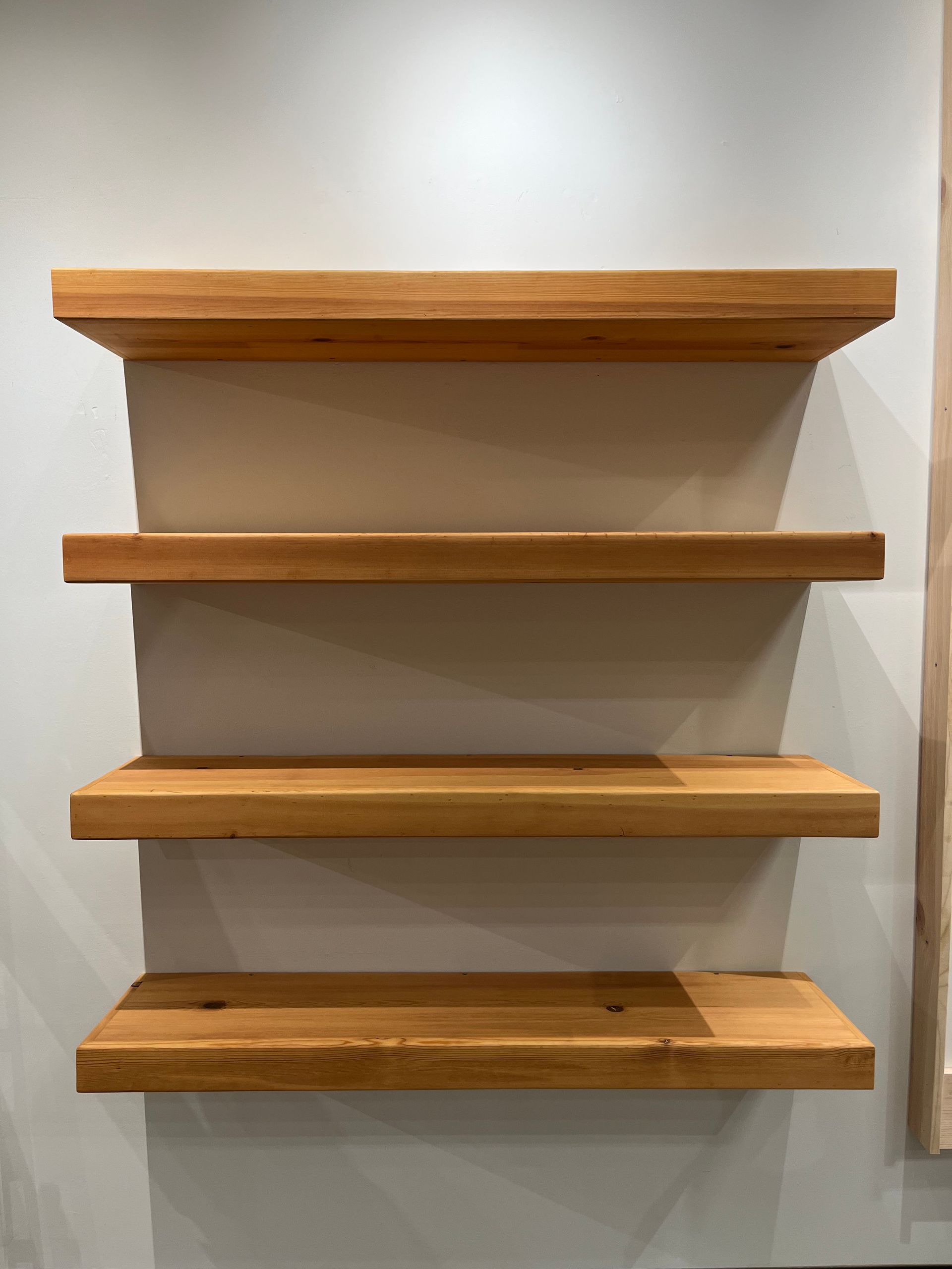 Four wooden floating shelves mounted against a plain light-colored wall.