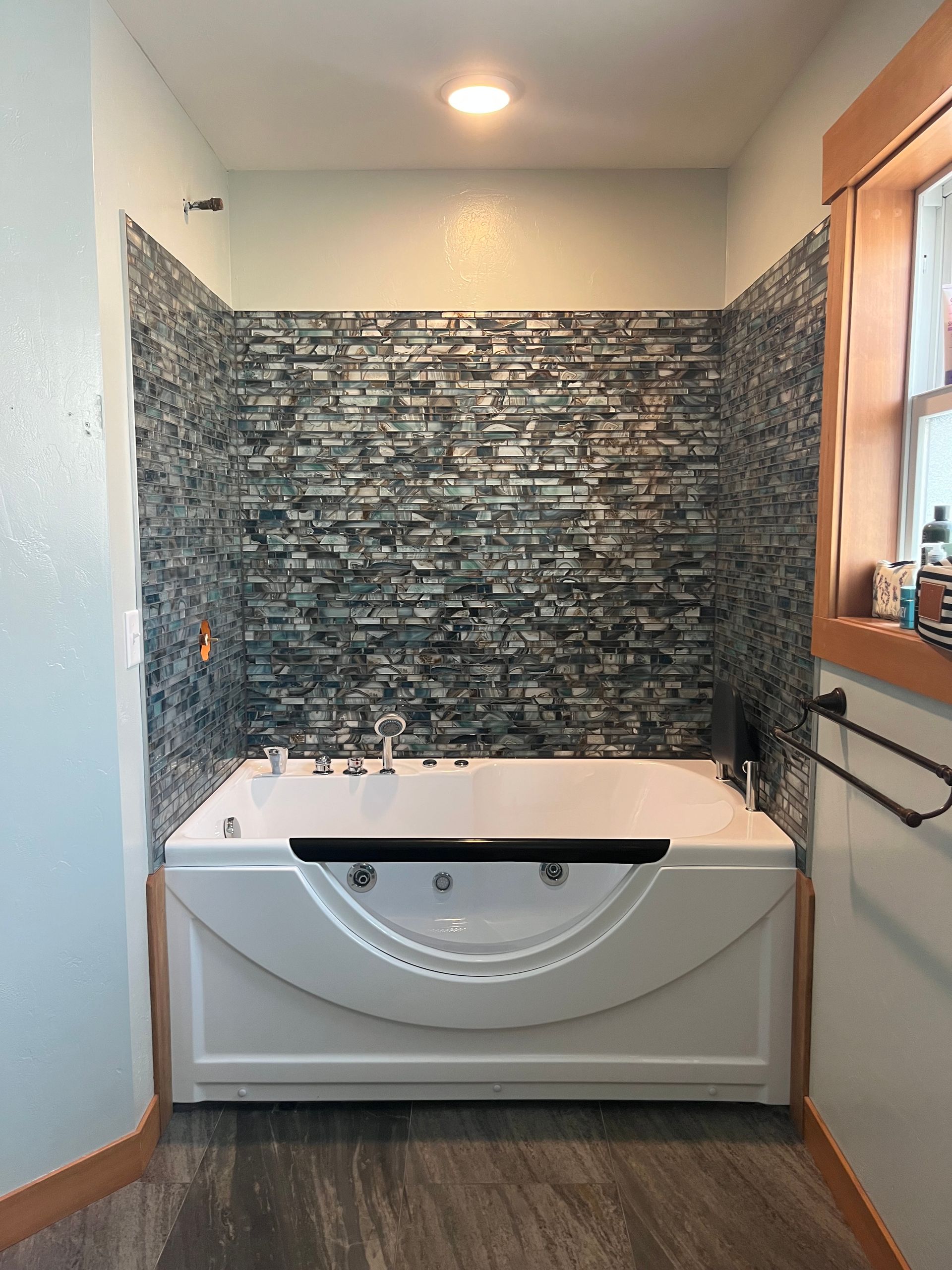A white jetted bathtub set against a textured, dark gray tiled accent wall in a bathroom with light blue walls.