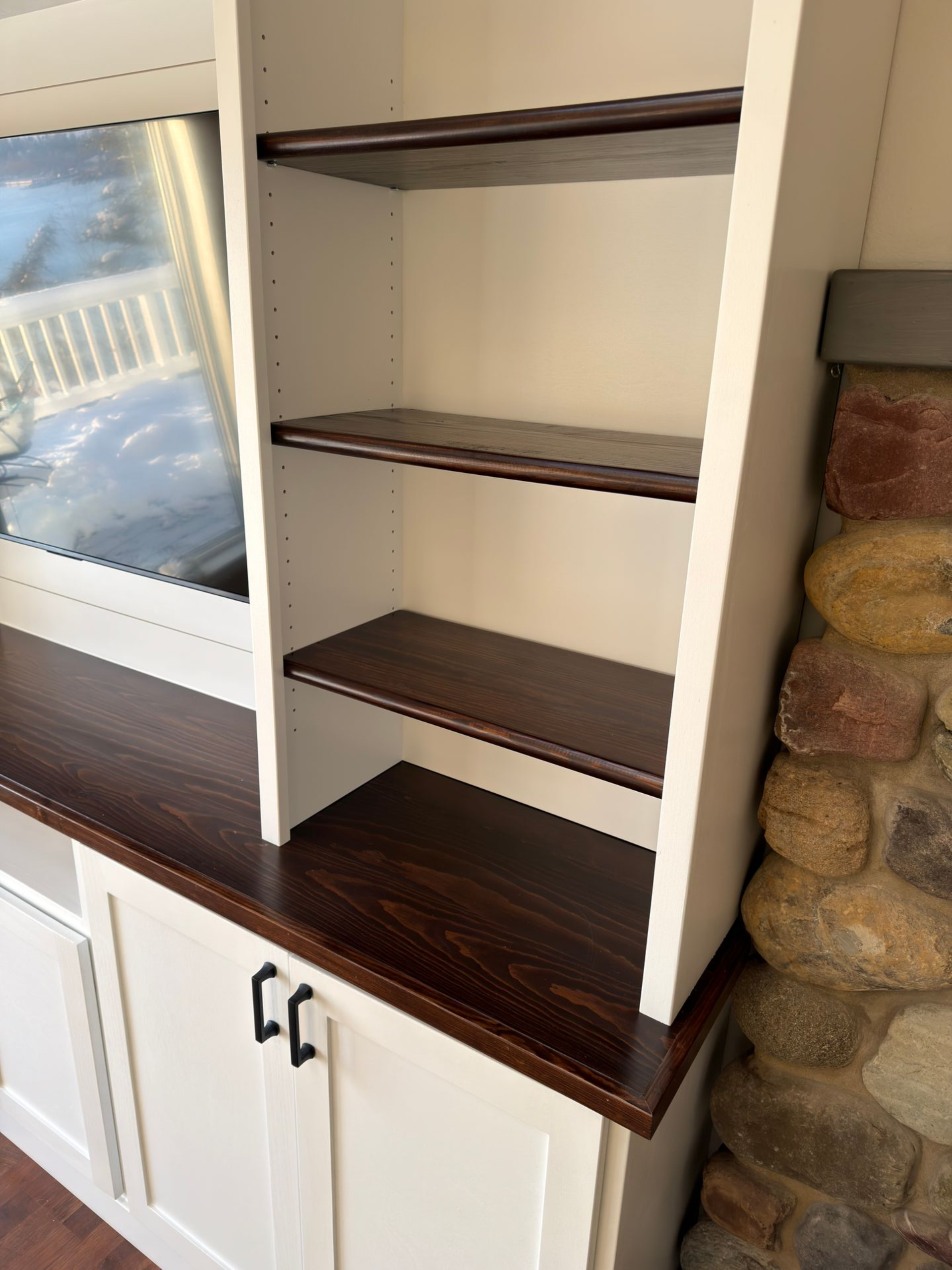 A custom white built-in cabinet with a dark wood countertop and three open shelves, situated next to a stone fireplace.