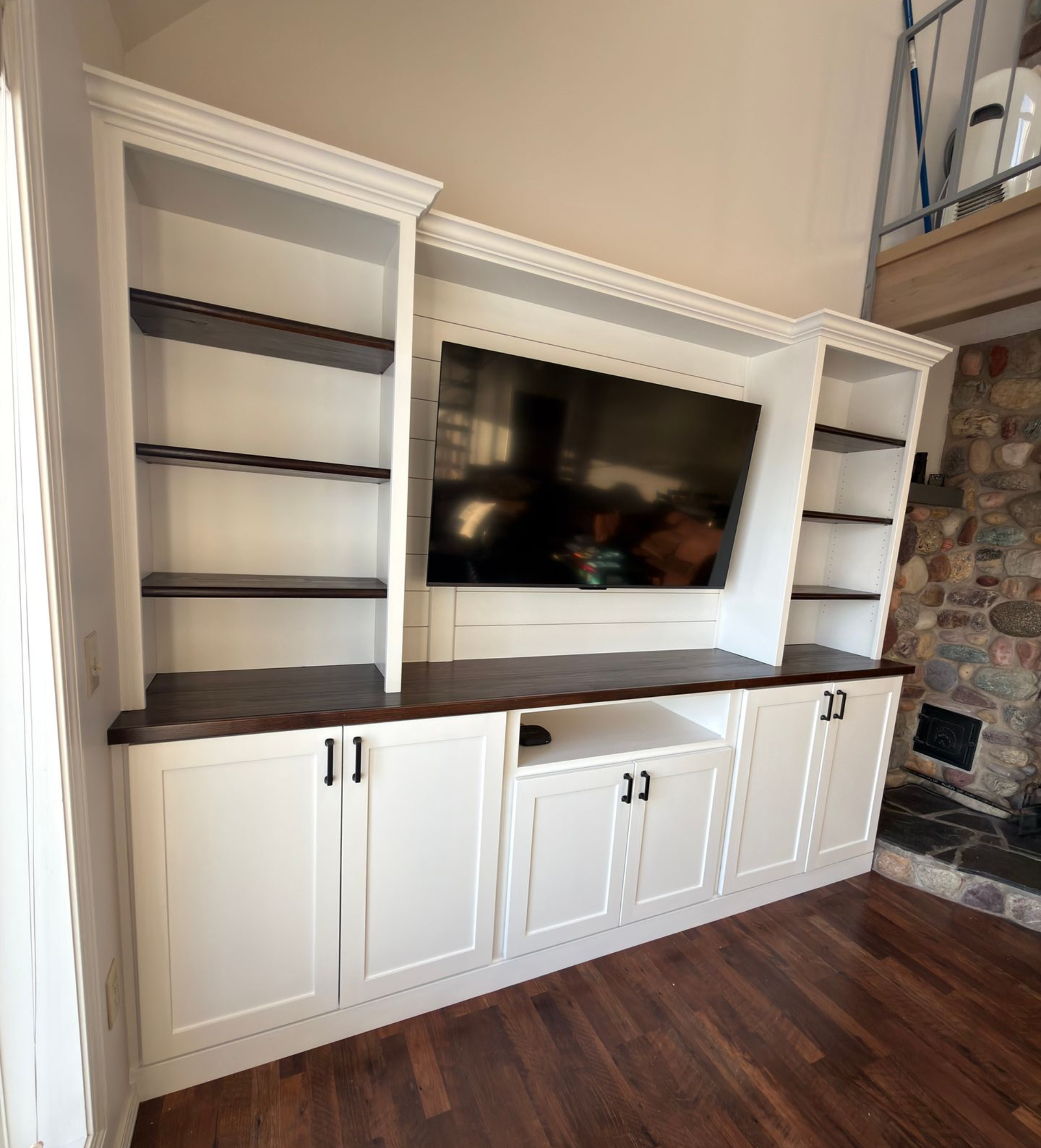 Custom white built-in cabinetry with dark wood shelving and countertops, framing a mounted television on a shiplap wall.