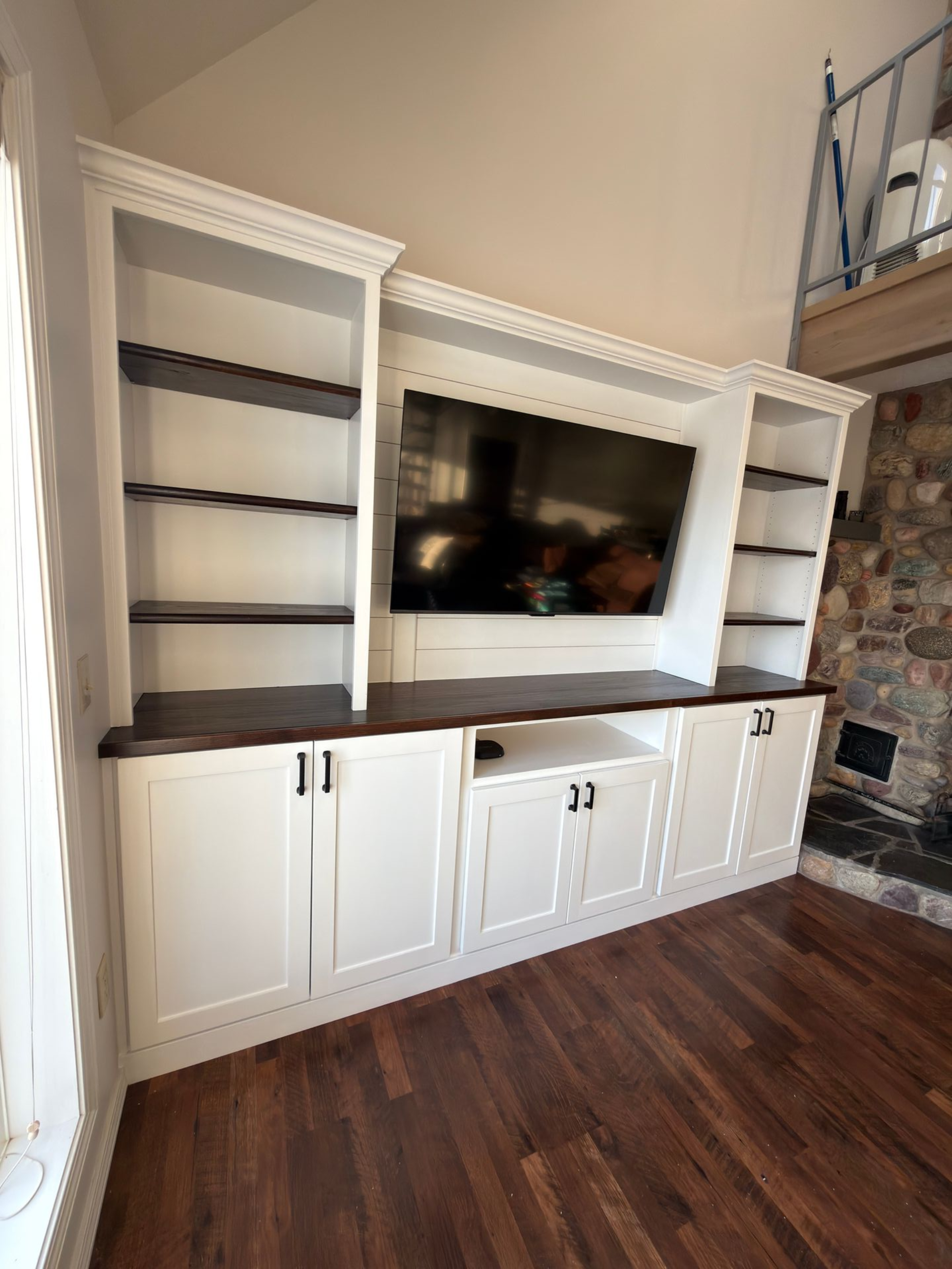 White built-in cabinetry with dark wood shelving and countertops surrounding a mounted television in a living room.