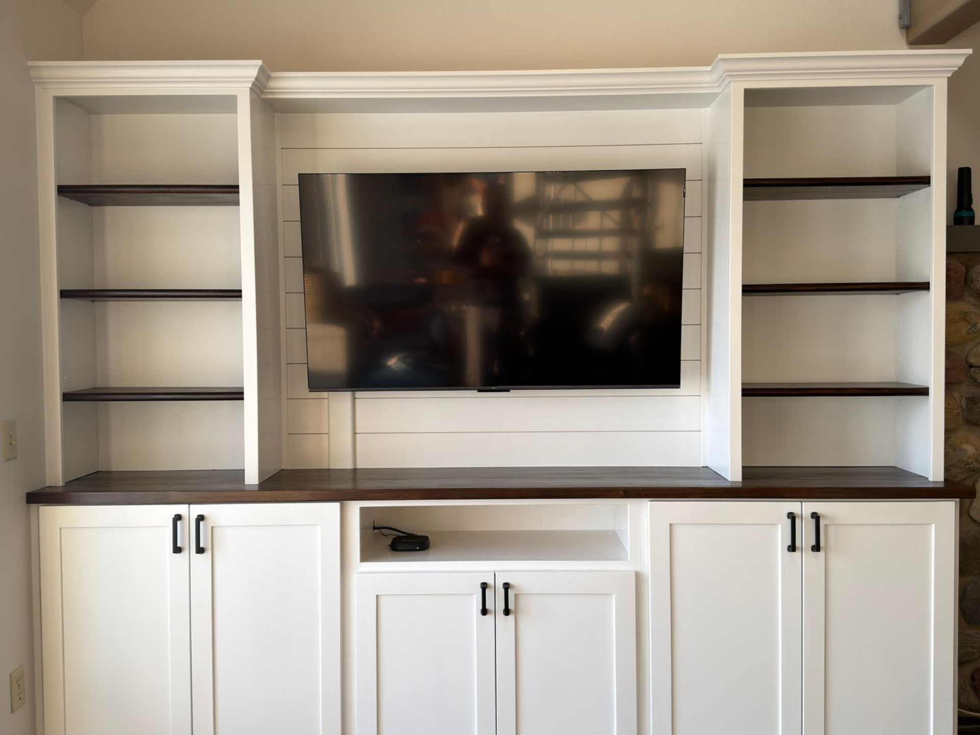 A white built-in entertainment center with a wall-mounted TV, open shelves with dark wood accents, and lower cabinet storage.