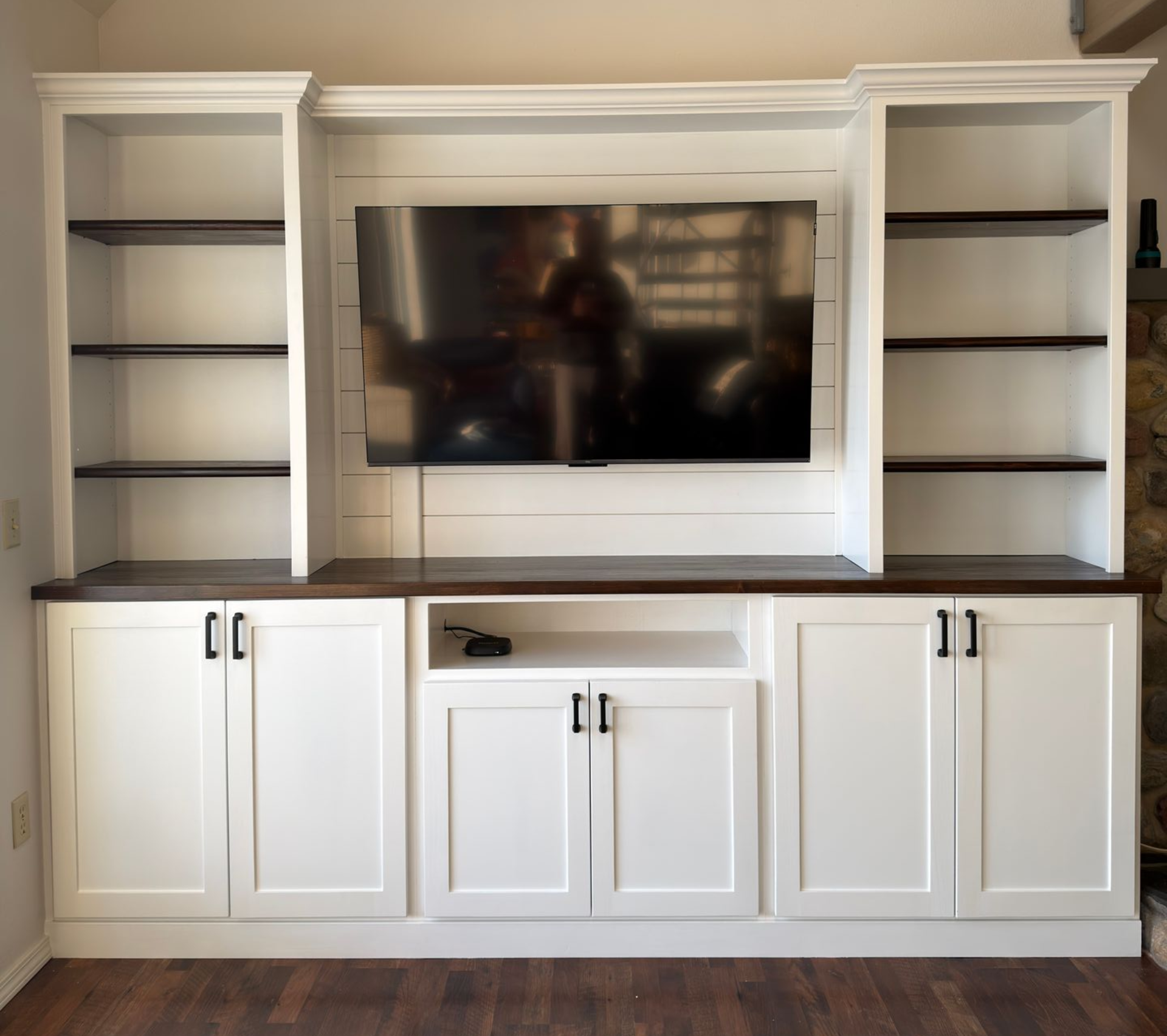 A white custom media center with a dark wood countertop, open shelving, lower cabinets, and a wall-mounted television.
