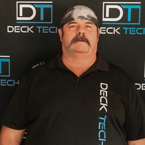 Man with a mustache wearing a black shirt and bandana, standing in front of a