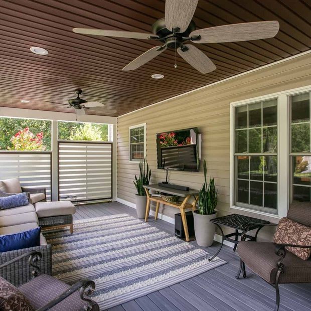 Covered porch with seating, rug, TV, and ceiling fans.