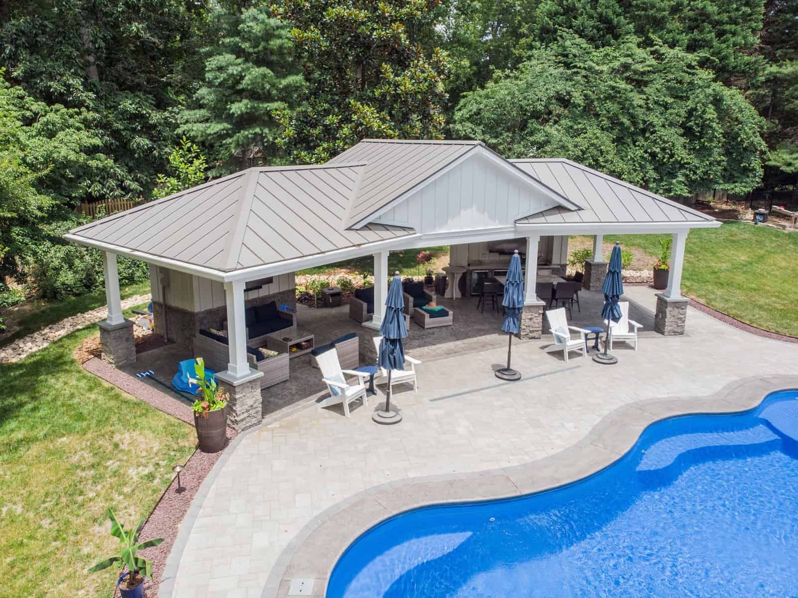 Poolside pavilion with gray roof, outdoor kitchen, seating, and blue pool.