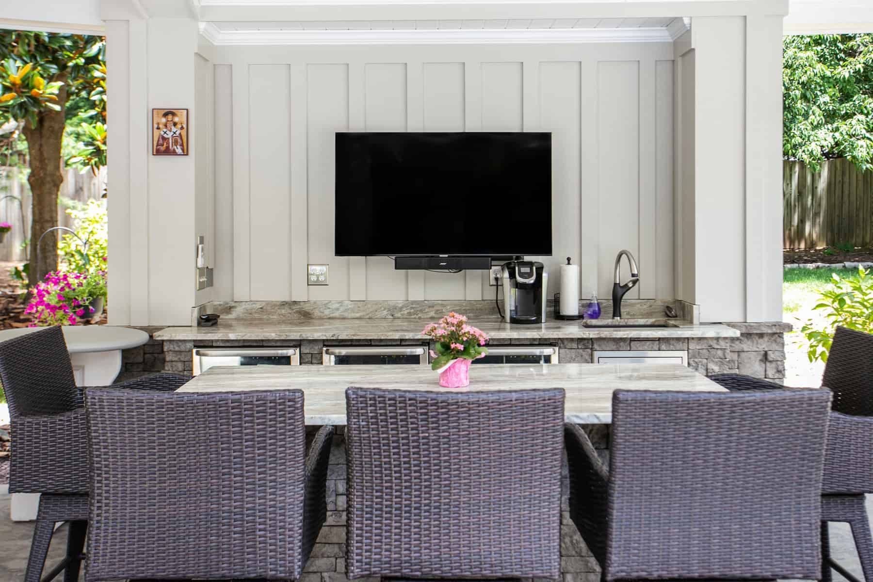 Outdoor entertainment space with TV, bar, seating, and a table with pink flowers.