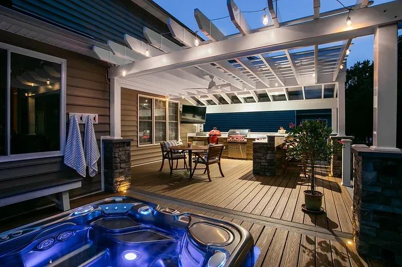 Outdoor deck with hot tub, pergola, seating, and grill at dusk.