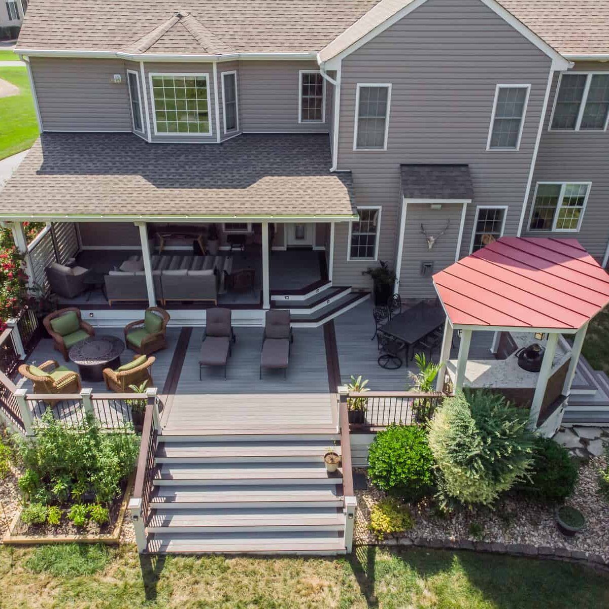 Backyard deck with gray siding house, stairs, seating, and red-roofed gazebo.