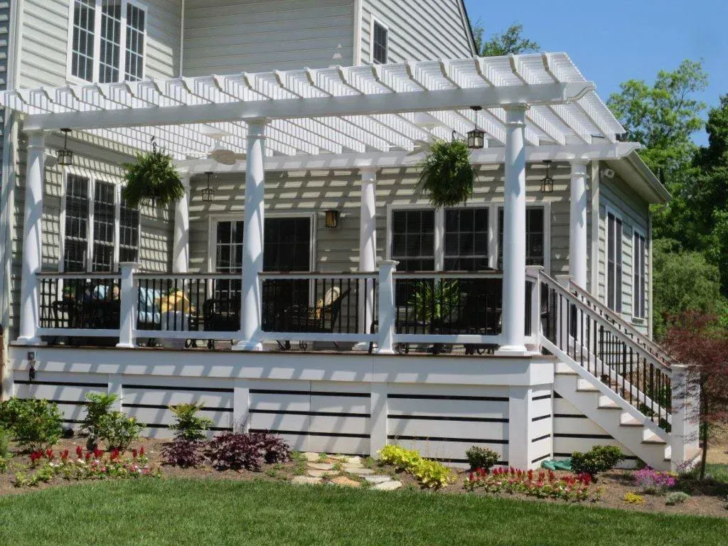 White pergola over a raised deck with stairs, featuring hanging plants and landscaping.