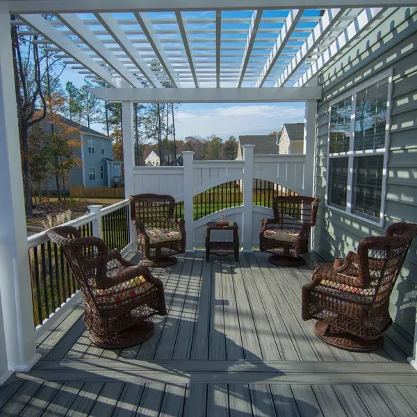 A deck with a white pergola, wicker chairs, and a small table. View of houses in the background.