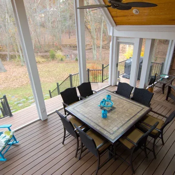 Screened porch with square table and black chairs, overlooking a wooded yard.