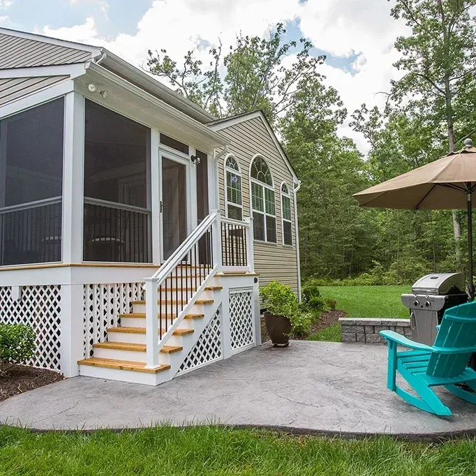 Backyard patio with screened porch, stairs, concrete, grill, turquoise chairs, and umbrella.