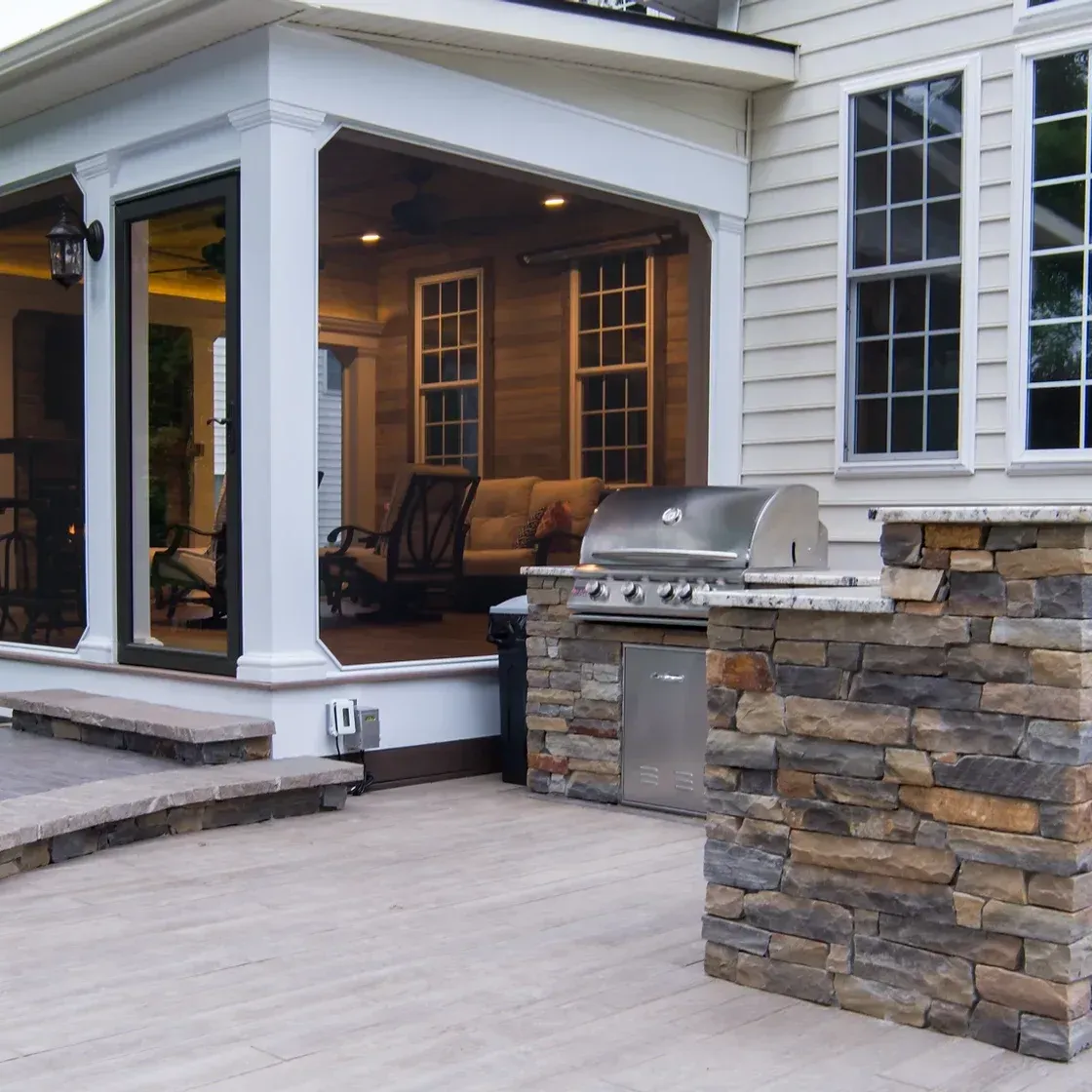Backyard patio with built-in grill, seating area under covered porch with wood siding, and stone accents.